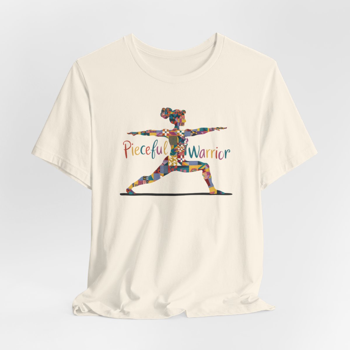 A Natural Tee featuring a colorful patchwork silhouette of woman in yoga warrior pose. Text reads "Pieceful Warrior" in multicolored lettering.