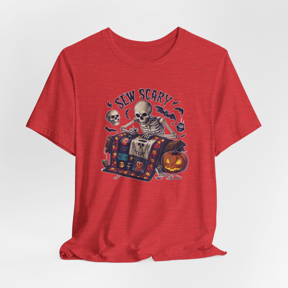 A Heather Red Halloween Quilting T-Shirt featuring a skeleton sewing Halloween quilt. Colorful patchwork with spooky motifs. Bats and pumpkins surround skeleton. Text reads "Sew Scary". Ideal for quilters who love Halloween.