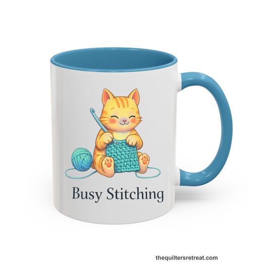 Crochet Gift: A Light Blue Ceramic Accent Mug with Cute cat crocheting with yarn ball, whimsical style, "Busy Stitching" text.