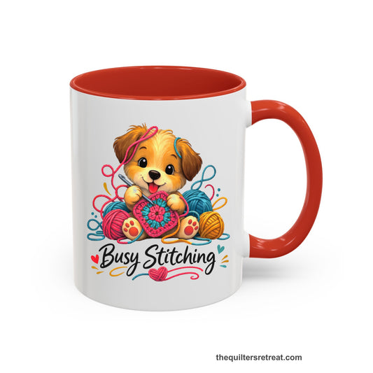 Crochet Gift: A Red Ceramic Accent Mug with Cute puppy crocheting with colorful yarn balls, whimsical style, "Busy Stitching" text.