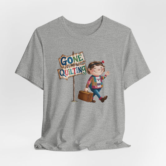 An Athletic Heatherfun quilting T-Shirt with a cartoon illustration of a smiling girl wearing a patchwork jacket, carrying a suitcase next to a wooden sign that reads "Gone Quilting" in colorful letters.