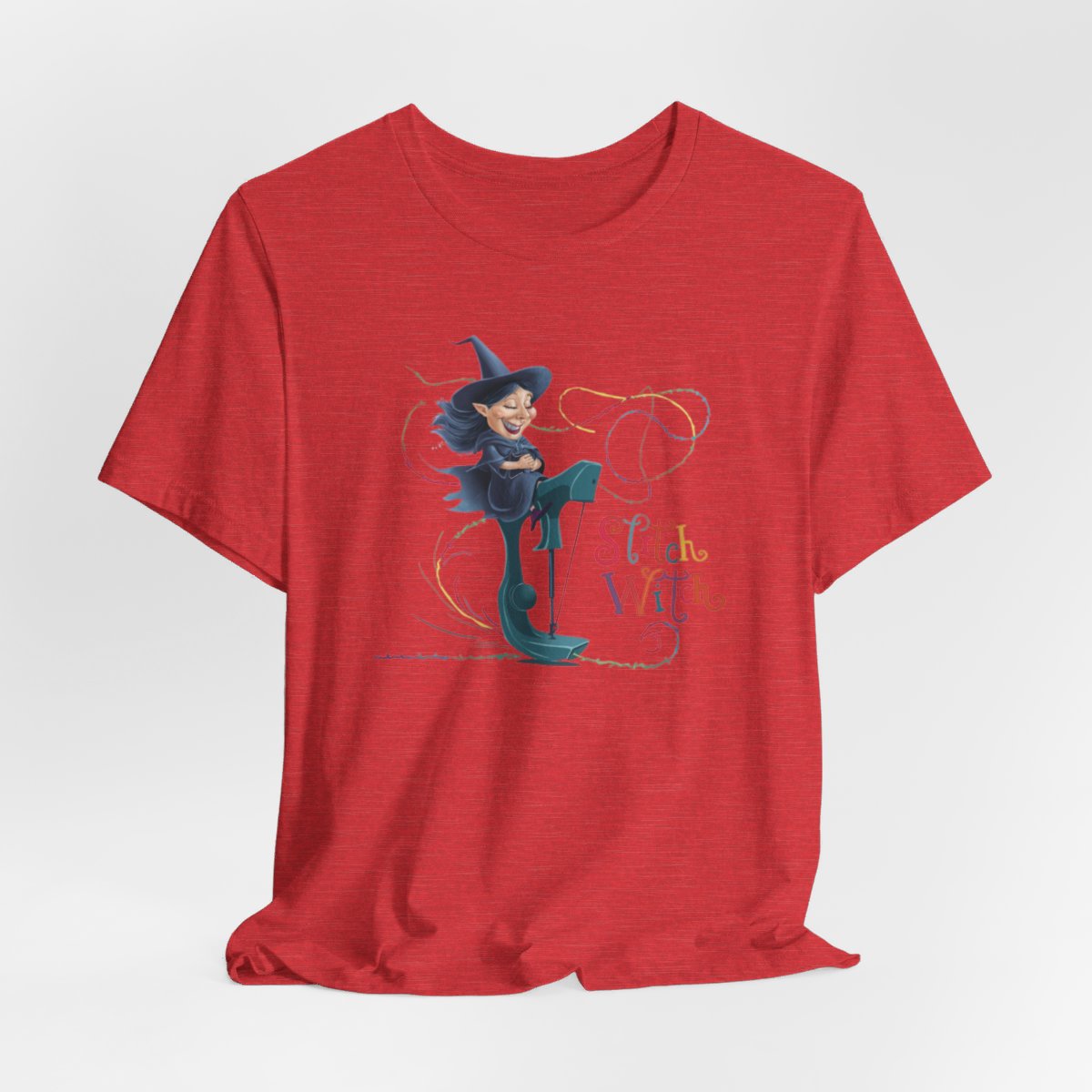 A Heather Red T-shirt with a cartoon illustration of a smiling witch with pointed hat riding a teal sewing machine. Colorful stitches swirl around her in the air. Text reads "Stitch Witch" in playful, multicolored letters.
