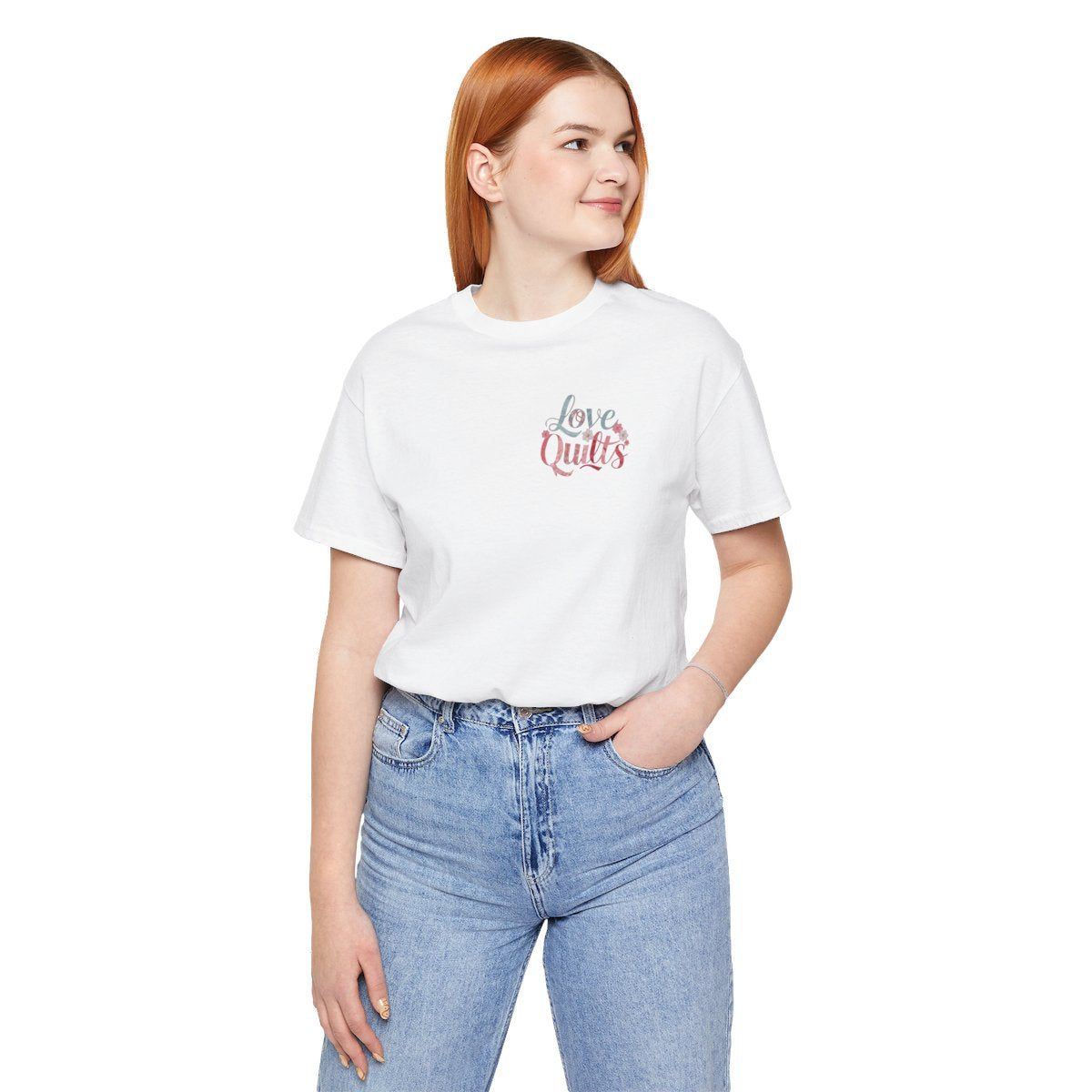 A White t-shirt spelling out "Love Quilts". The word "Love" is in teal, while "Quilts" features various shades of pink and red. Small flowers in white and pink adorn the letters, creating a floral and quilting-inspired artwork.