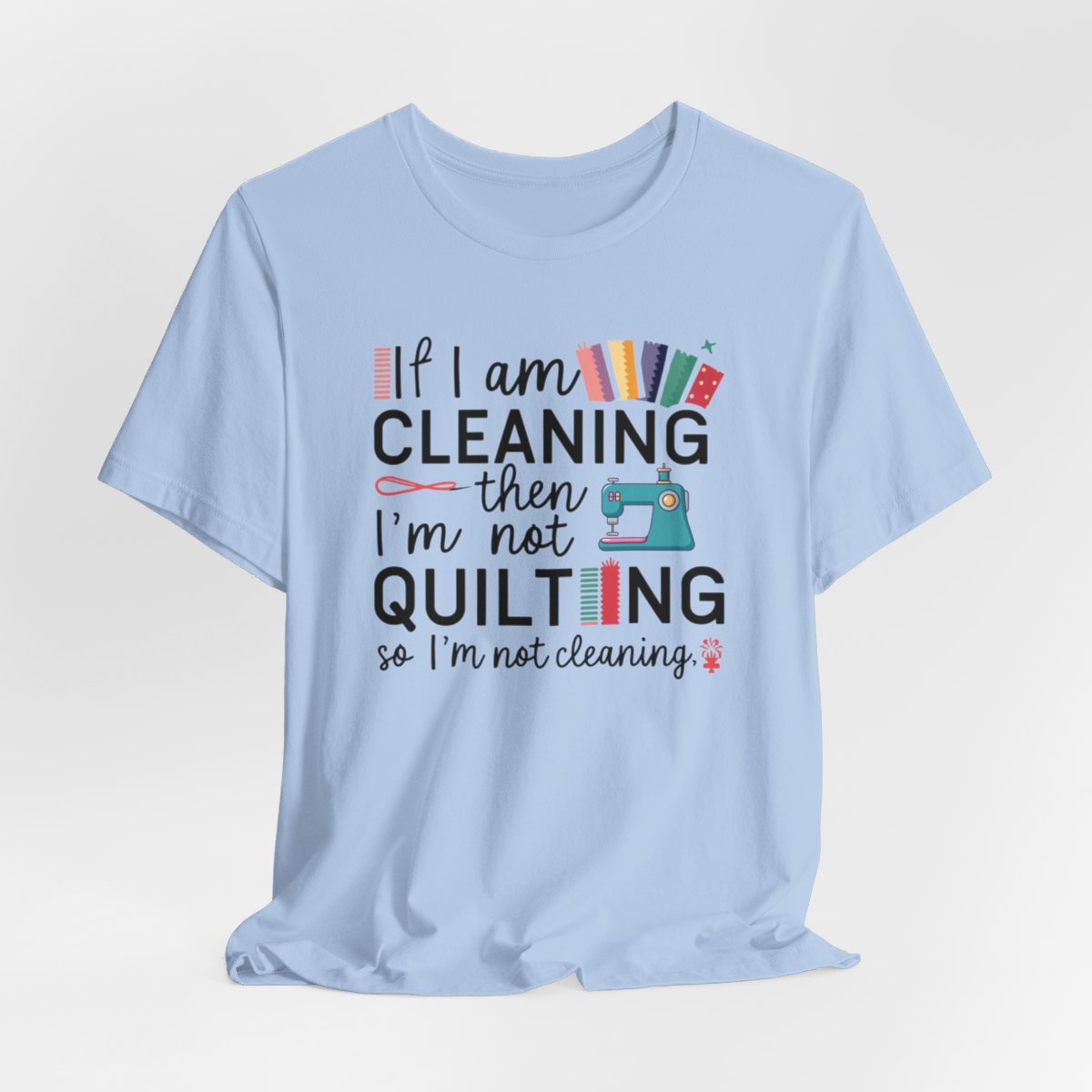 A Baby Blue funny quilting T-Shirt with the phrase If I am Cleaning then I'm not Quilting in a bold and cheerful font with images of quilting icons and supplies