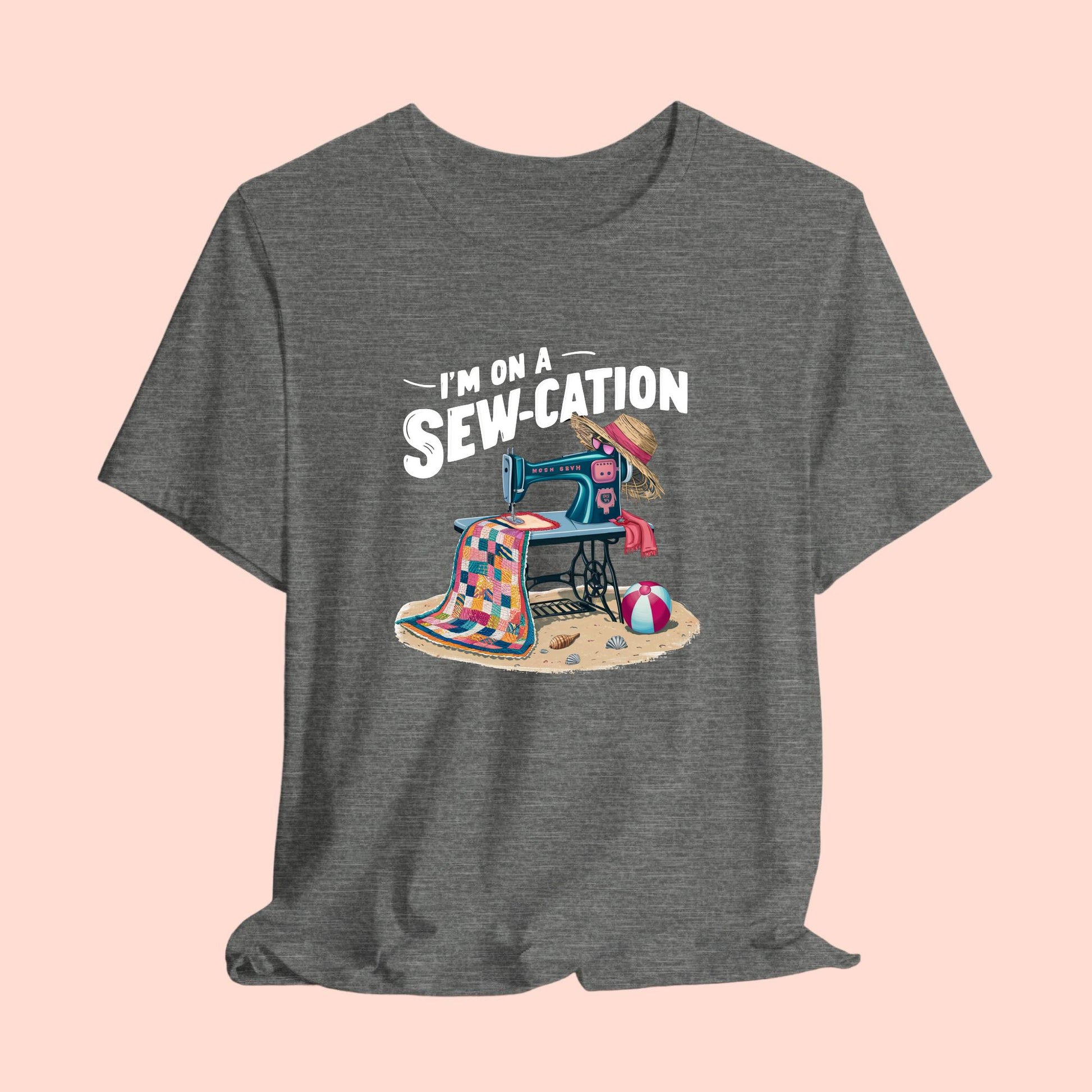A fun Quilting T-shirt of a vintage sewing machine on a beach with a colorful quilt, sun hat, and beach ball. Text above reads "I'm on a Sew-cation" in bold letters.