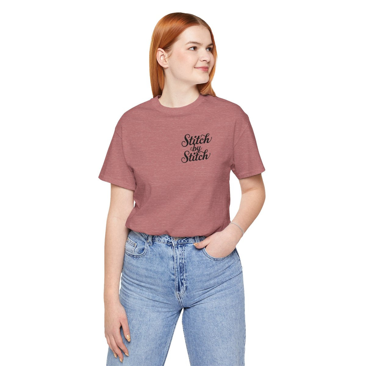 A Heather Mauve T-Shirt featuring the phrase "Stitch by Stitch". The word "Stitch" is written twice in a flowing script font, while "by" is centered between them in a smaller, sans-serif font. The design has a clean, minimalist aesthetic.