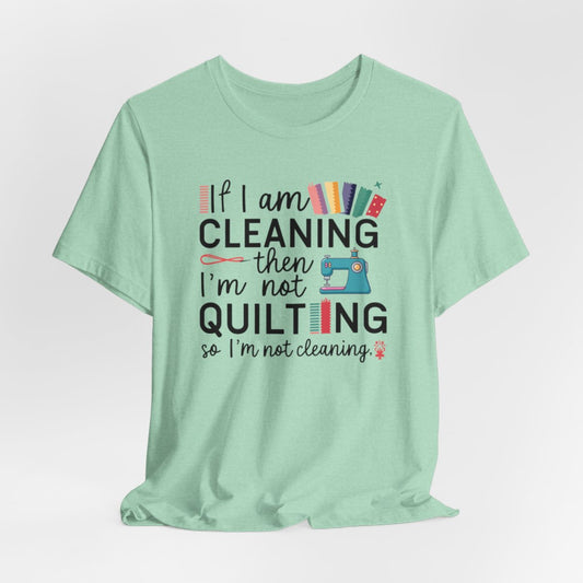 A Heather Mint funny quilting T-Shirt with the phrase If I am Cleaning then I'm not Quilting in a bold and cheerful font with images of quilting icons and supplies