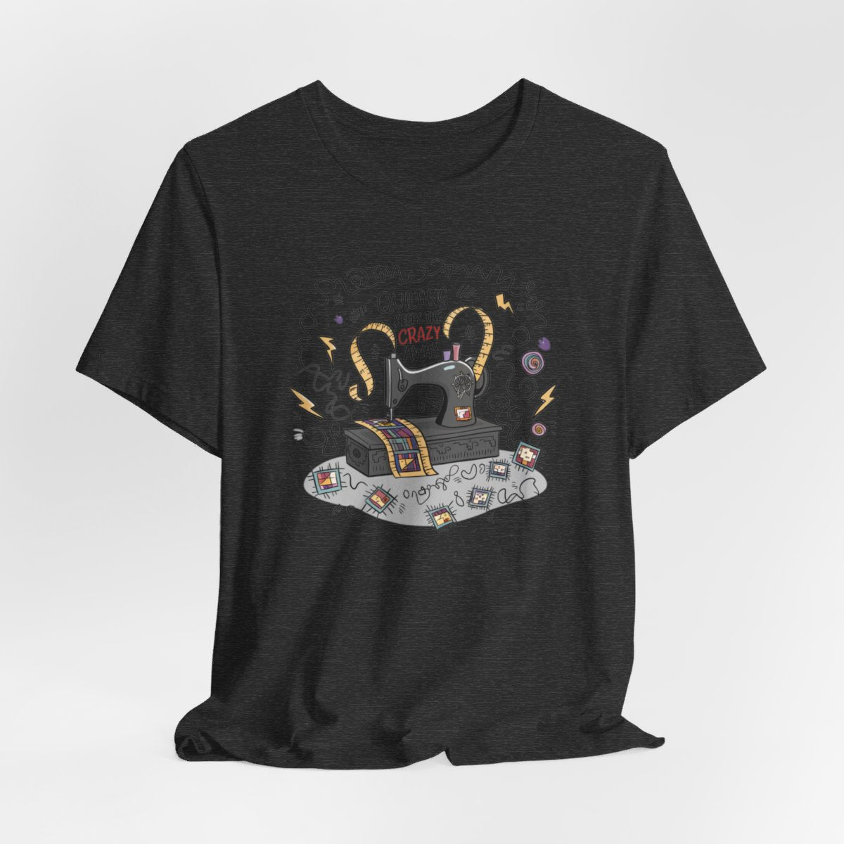 A Dark Grey Heather T-Shirt with a vintage sewing machine, measuring tape heart, and text "Quilting Keeps the Crazy Away" amidst swirls and quilting motifs.