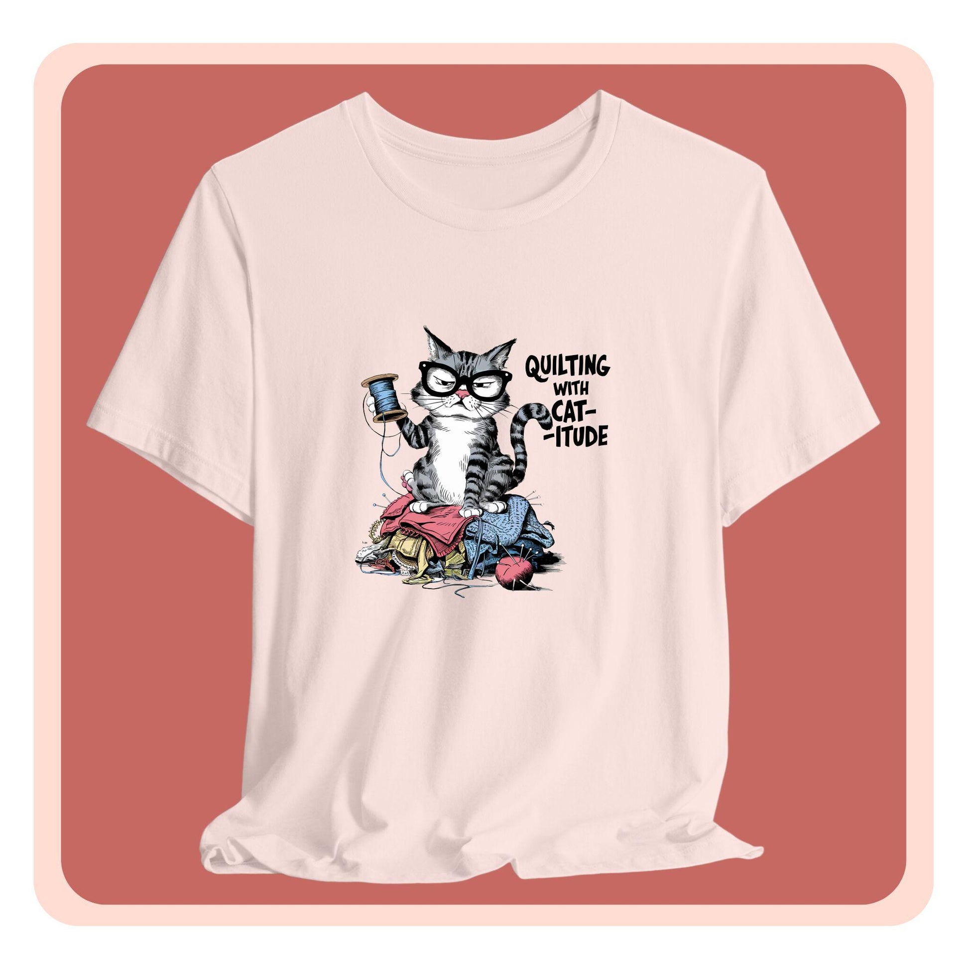 A t-shirt featuring a sassy cartoon cat sitting on a pile of colorful fabric, holding a spool of thread, with the phrase 'Quilting with Cat-itude,' perfect for quilters and cat lovers.