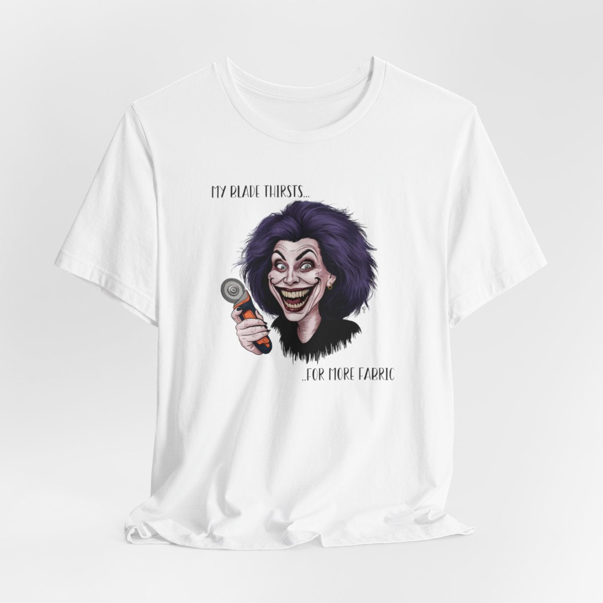 A White T-shirt showing a cartoonish character with wild purple hair and an exaggerated grin, holding a rotary cutter. Text reads "My blade thirsts... for more fabric", humorously depicting a quilter's endless desire for new materials.