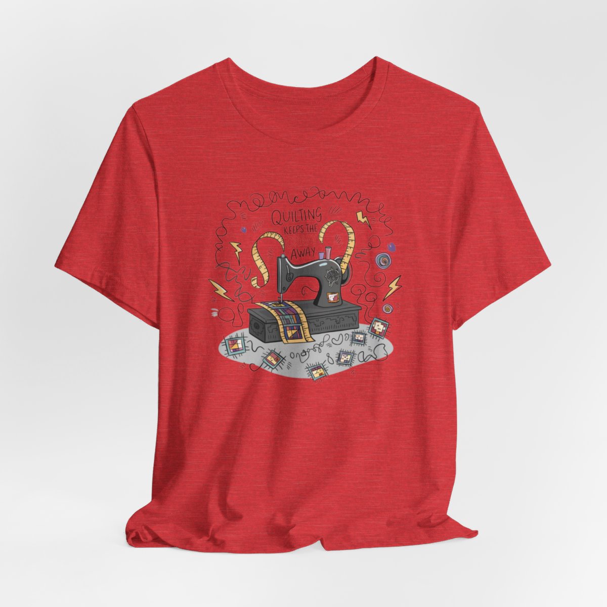 A Heather Red T-Shirt with a vintage sewing machine, measuring tape heart, and text "Quilting Keeps the Crazy Away" amidst swirls and quilting motifs.