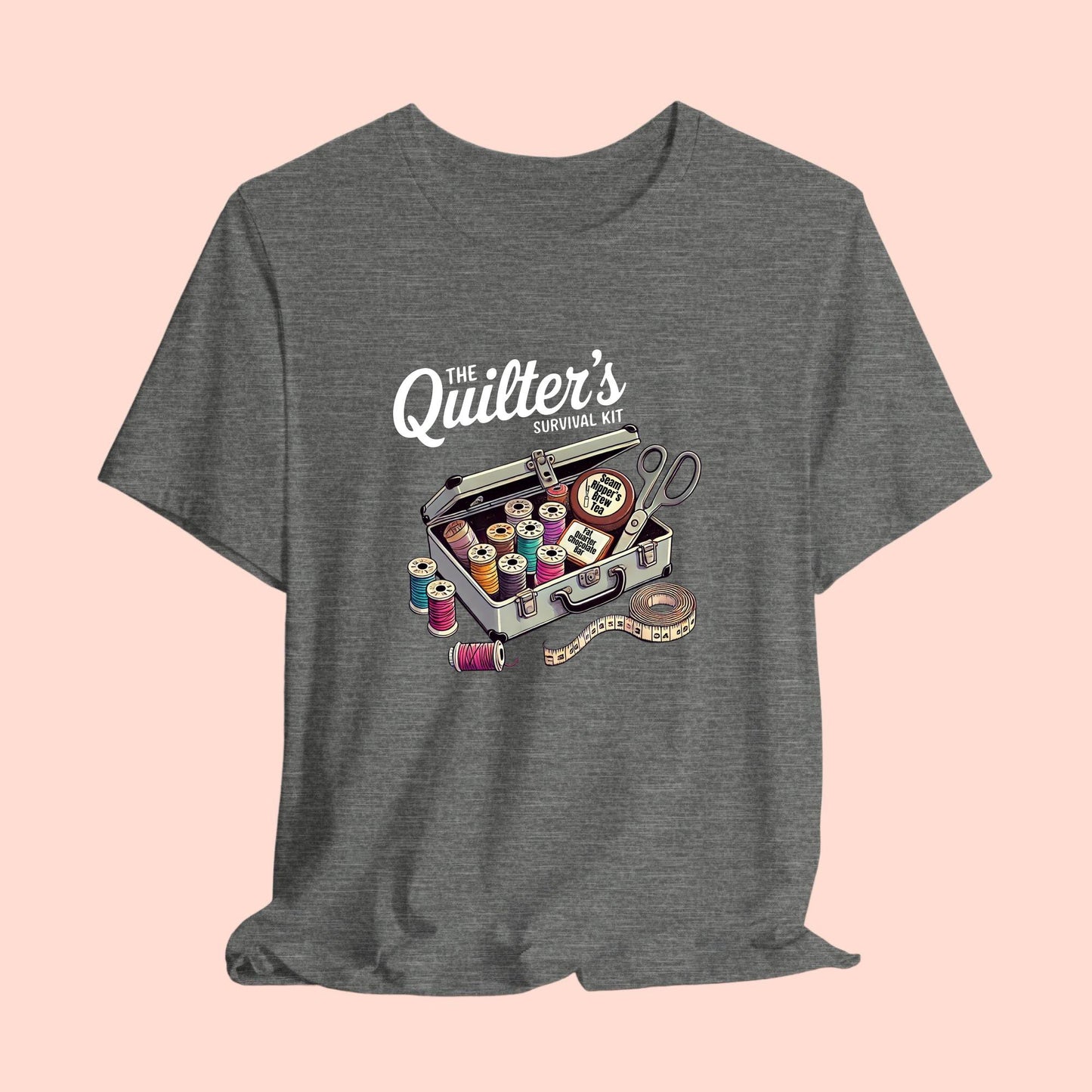 A t-shirt featuring a whimsical illustration of a quilter’s survival kit with colorful thread spools, scissors, and a tape measure, perfect for sewing and quilting enthusiasts.