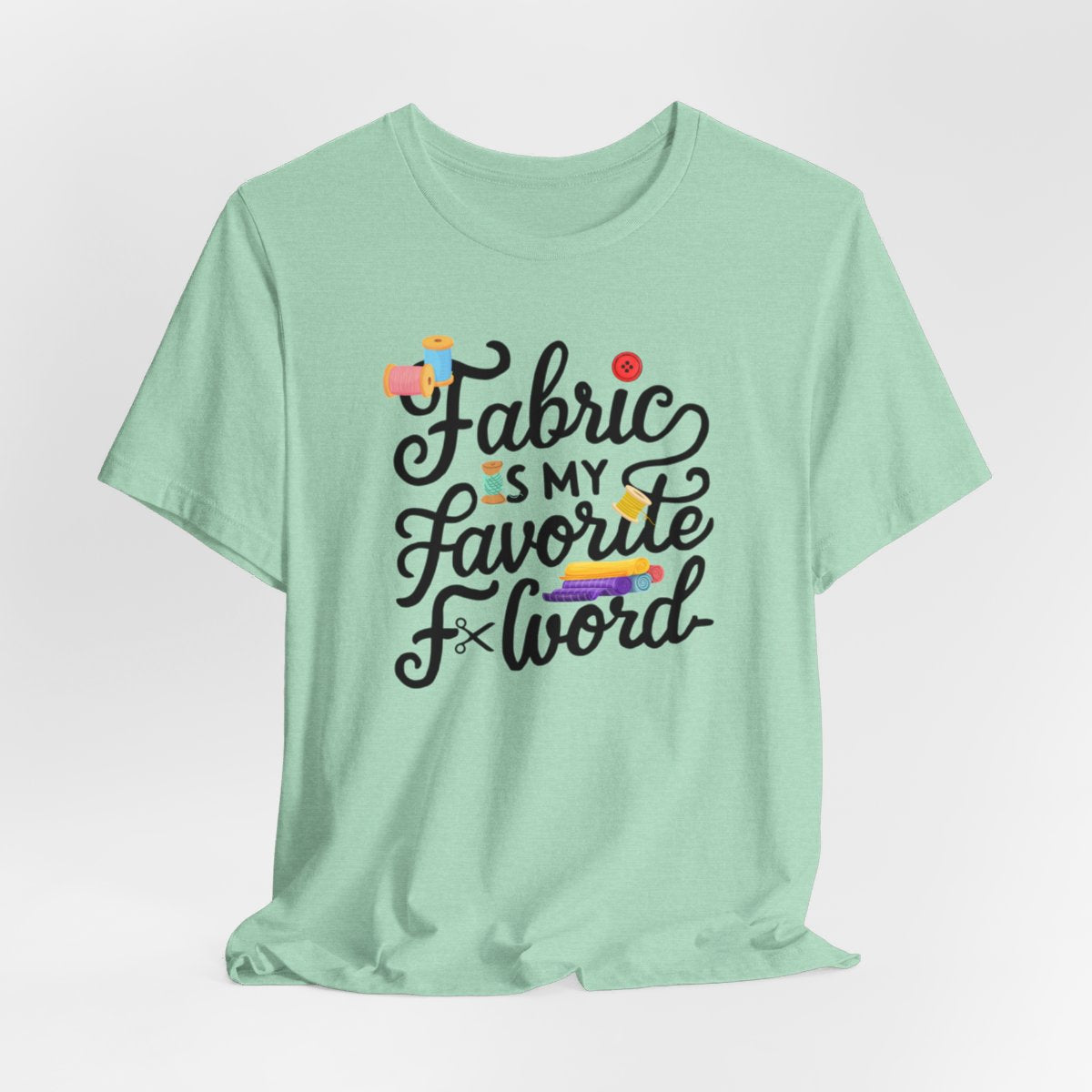 A Heather Mint T-Shirt with the phrase Fabric is My Favorite F-Word in a bold font with thread, buttons, and fabric bolts
