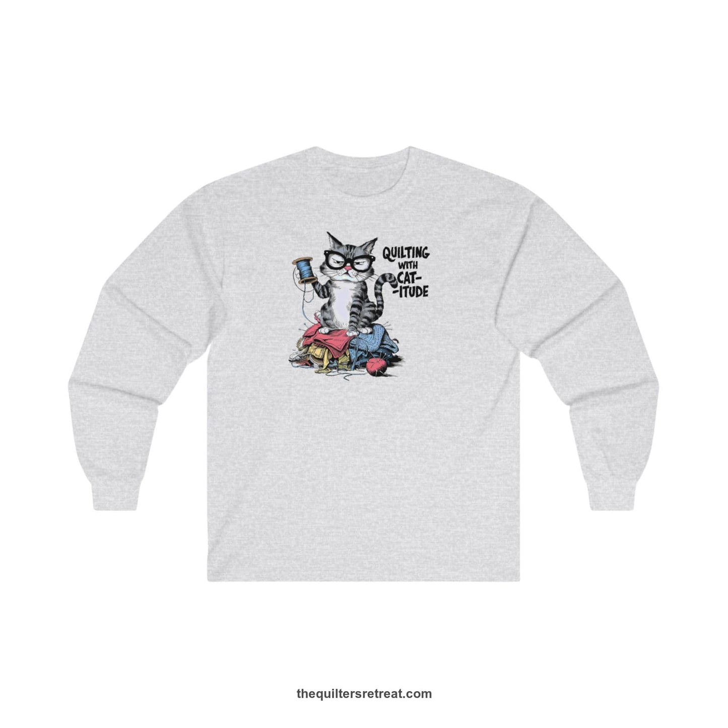 A Ash Long Sleeve T-Shirt with a grumpy cat holding thread spool atop fabric pile with "Quilting with Cat-itude" text