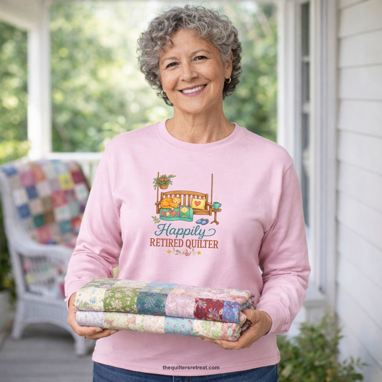 A Long Sleeve T-Shirt with a hanging bench with cozy cat and quilt, surrounded by plants, "Happily Retired Quilter" text