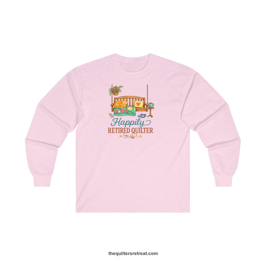 A Long Sleeve T-Shirt with a hanging bench with cozy cat and quilt, surrounded by plants, "Happily Retired Quilter" text