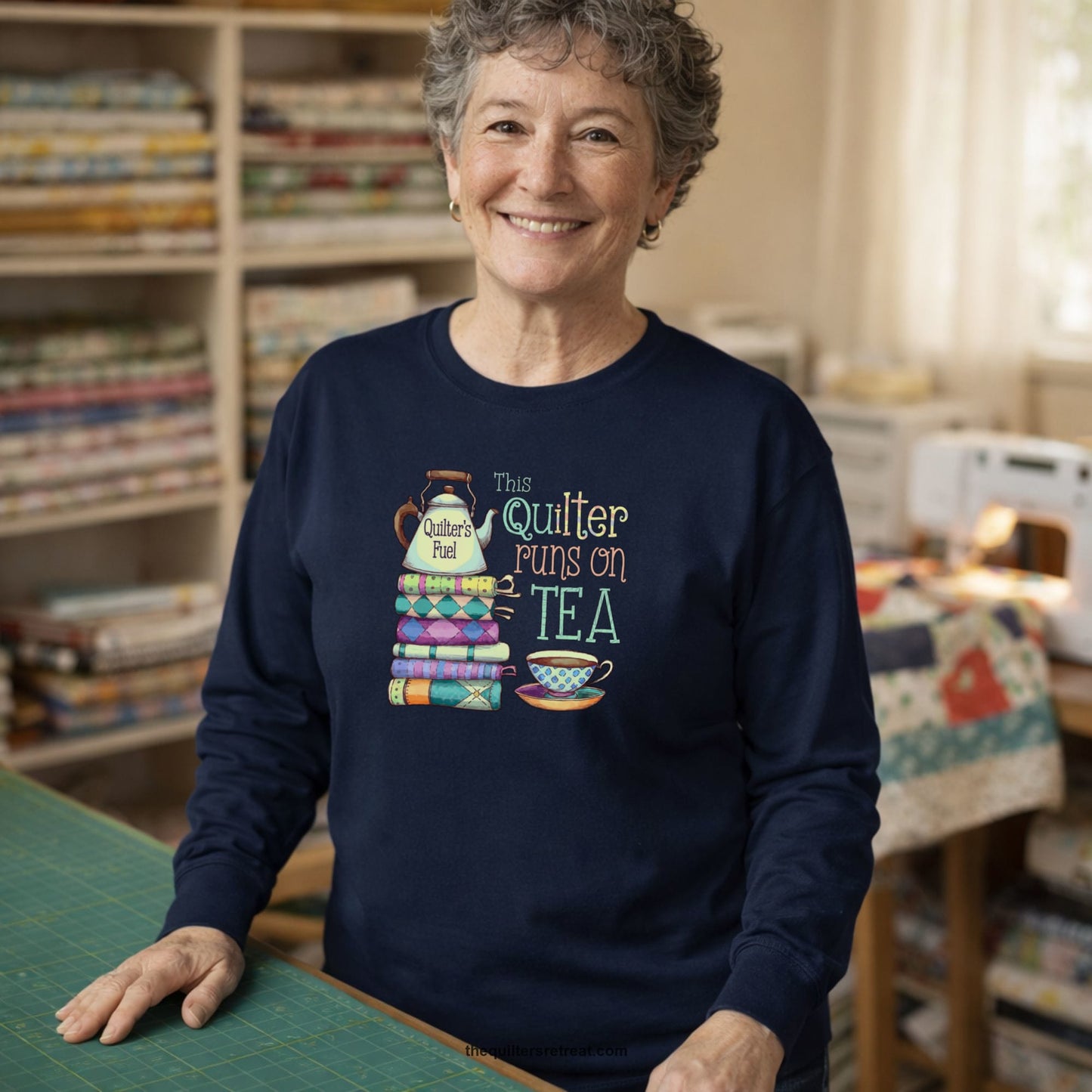 A Long Sleeve T-Shirt with a stack of colorful quilts with teapot and cup, whimsical "This Quilter Runs on Tea" text