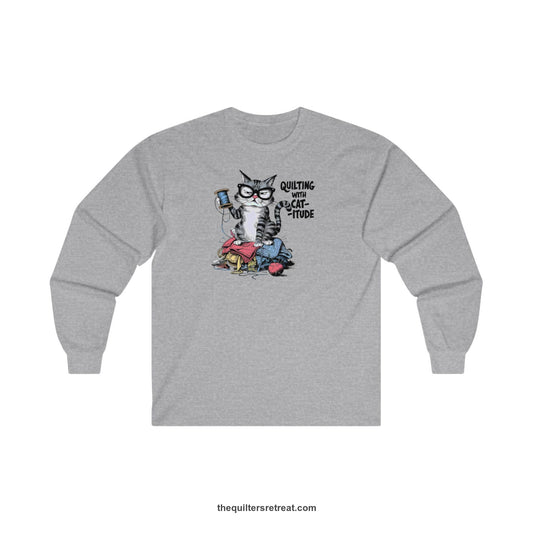A Long Sleeve T-Shirt with a grumpy cat holding thread spool atop fabric pile with "Quilting with Cat-itude" text