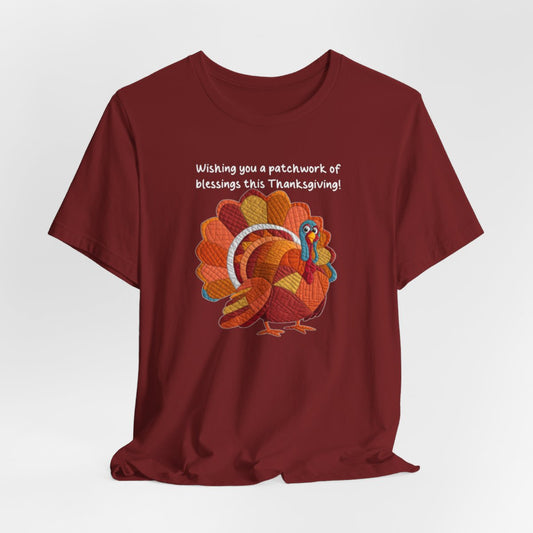 A Cardinal thanksgiving quilting t-shirt featuring a quilted patchwork turkey in autumn colors with text "Wishing you a patchwork of blessings this Thanksgiving!" Turkey features various quilt patterns and textures in shades of orange, red, yellow, and blue. Whimsical, crafty holiday design perfect for quilting enthusiasts.