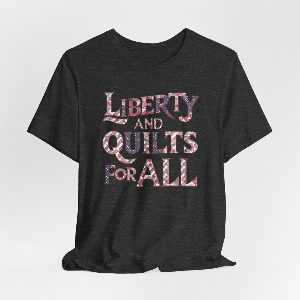 A Dark Grey Heather T-shirt featuring text "LIBERTY AND QUILTS FOR ALL" in large decorative letters filled with various quilt patterns in red, white, and blue.