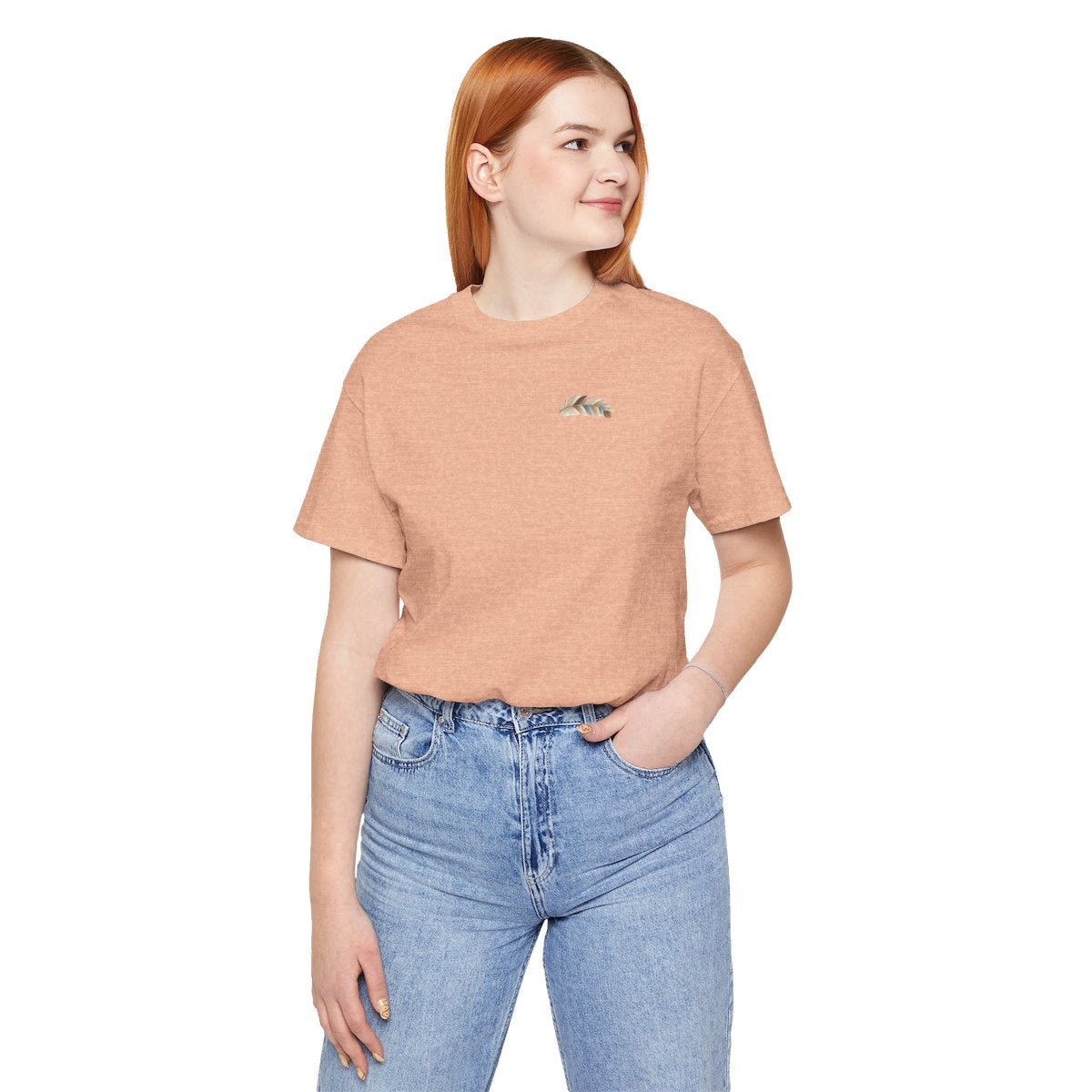 A Heather Peach T-Shirt featuring an illustration of a curving feather simulating patterned sections, resembling a patchwork quilt. The feather features a mix of floral, polka dot, and geometric designs in shades of blue, brown, and pink, with a dotted line tracing its path.