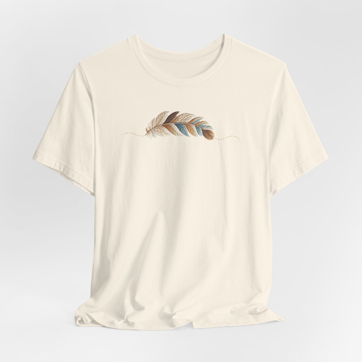 A Natural T-Shirt with an illustration of a curving feather simulating patterned sections, resembling a patchwork quilt. The feather features a mix of floral, polka dot, and geometric designs in shades of blue, brown, and pink, with a dotted line tracing its path.