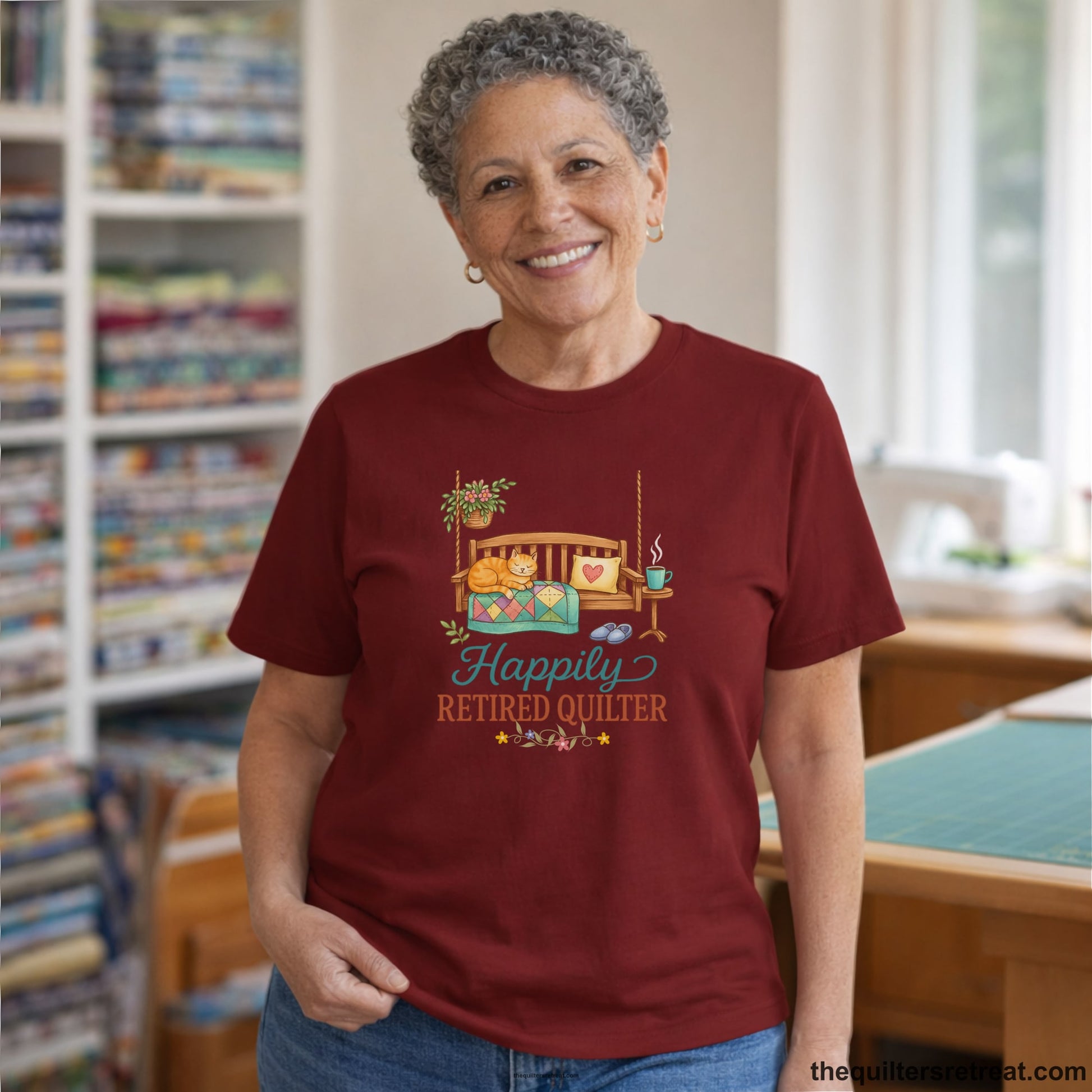 A Short Sleeve T-Shirt with a hanging bench with cozy cat and quilt, surrounded by plants, "Happily Retired Quilter" text