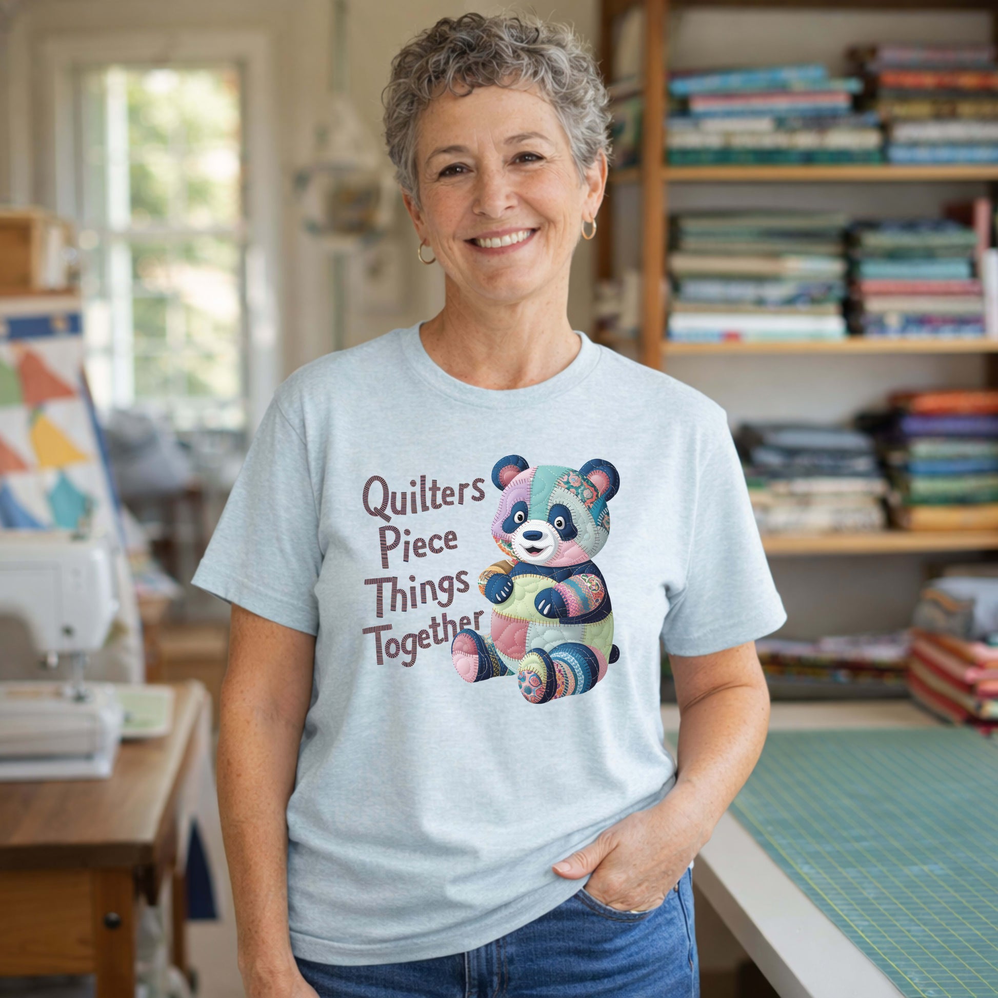 A Heather Ice Blue Short Sleeve T-Shirt with a patchwork panda with "Quilters Piece Things Together" text in a whimsical style