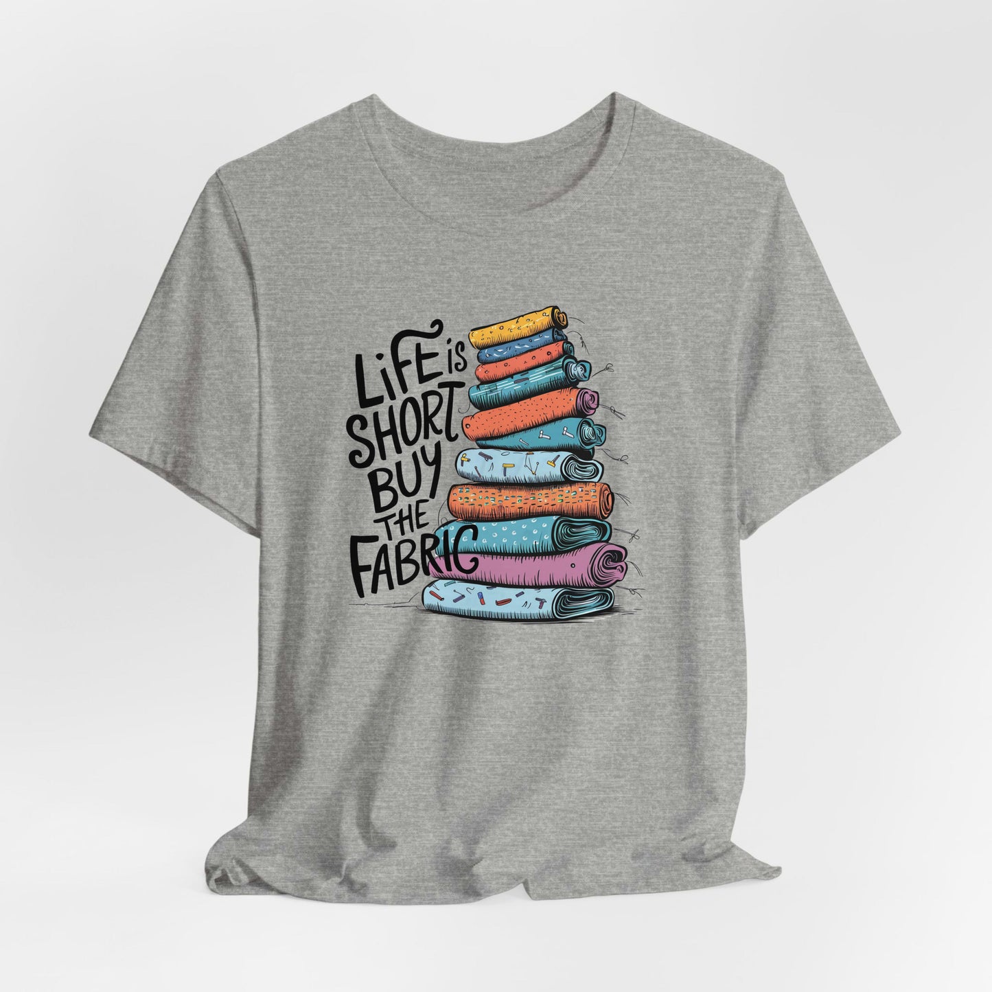 A Athletic Heather Short Sleeve T-Shirt with a illustration of colorful fabric rolls with bold "Life is Short Buy the Fabric" text