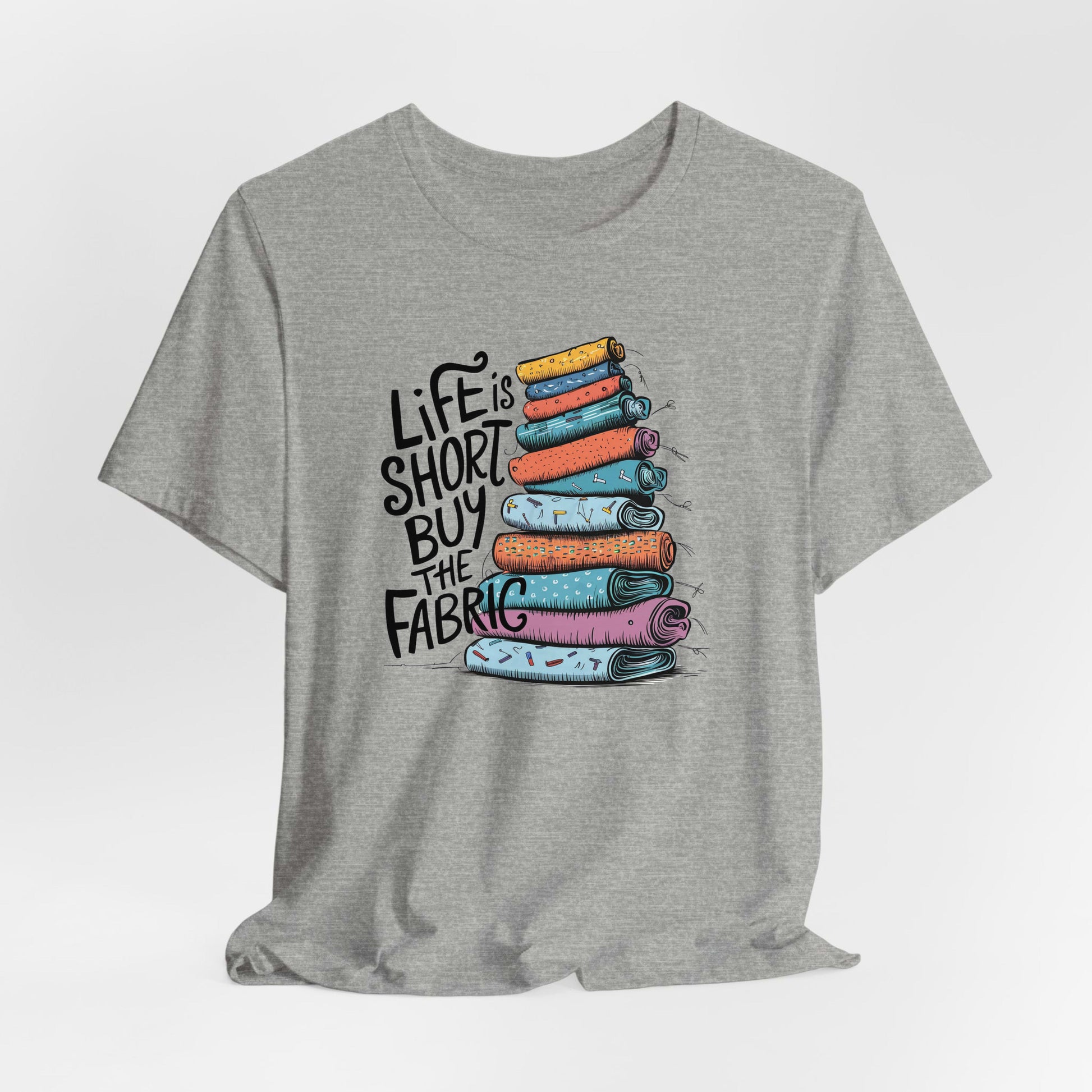 A Athletic Heather Short Sleeve T-Shirt with a illustration of colorful fabric rolls with bold "Life is Short Buy the Fabric" text