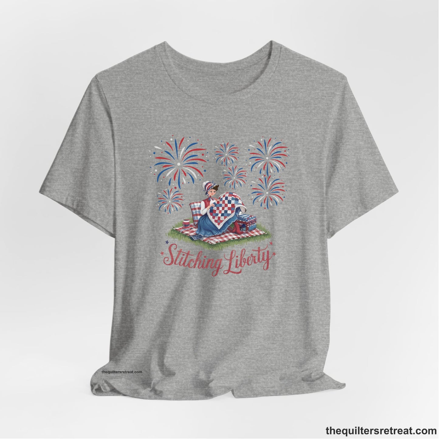 A Athletic Heather Short Sleeve T-Shirt with a vintage illustration of woman quilting with fireworks and "Stitching Liberty" text in patriotic style