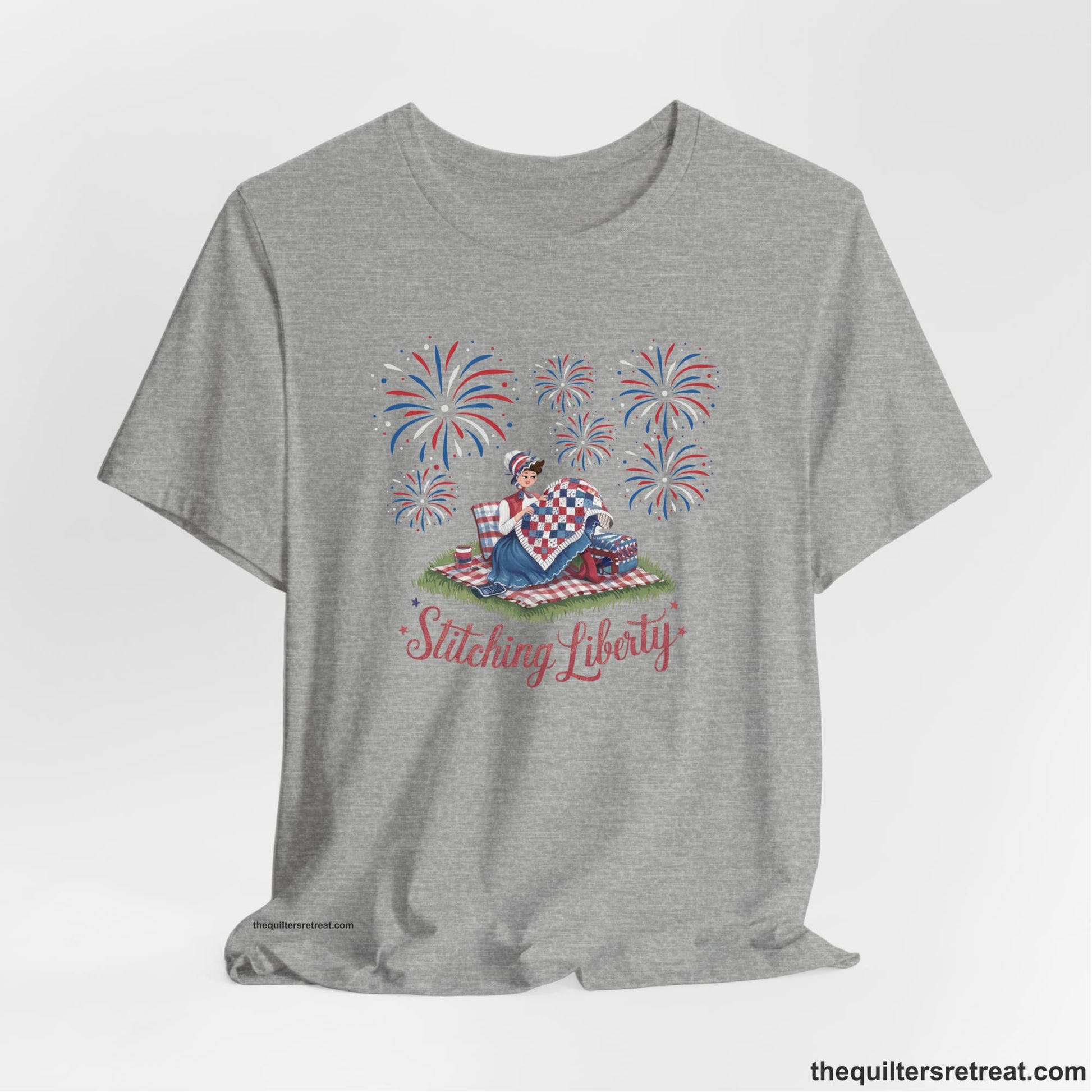 A Athletic Heather Short Sleeve T-Shirt with a vintage illustration of woman quilting with fireworks and "Stitching Liberty" text in patriotic style
