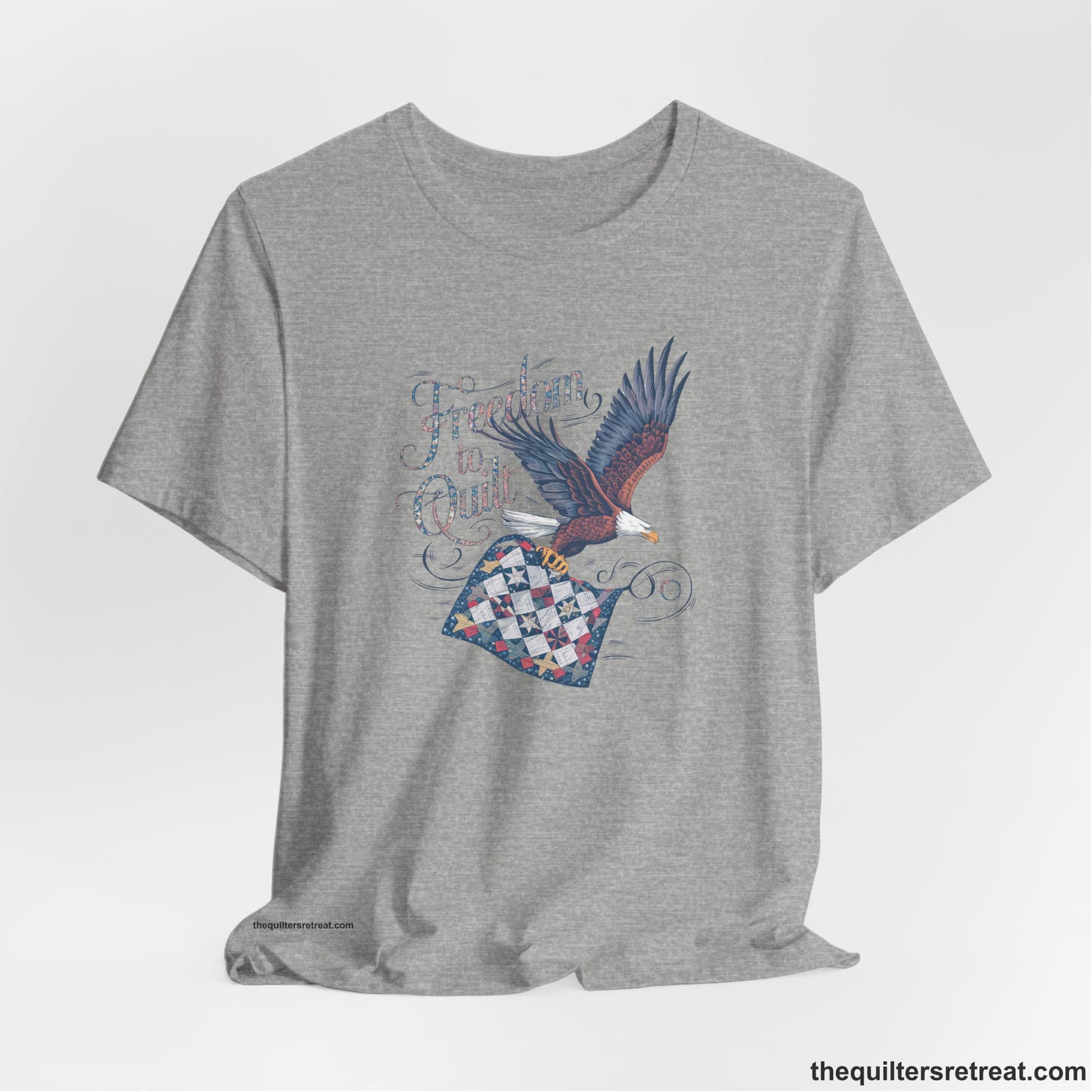 A Athletic Heather Short Sleeve T-Shirt with a freedom to quilt text with an eagle carrying a colorful patchwork quilt in vintage style