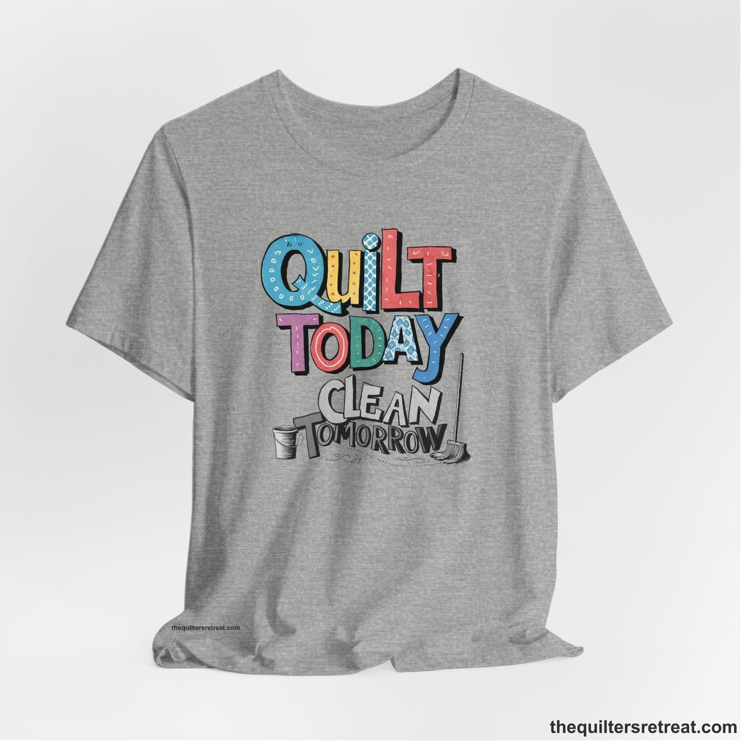 A Athletic Heather Short Sleeve T-Shirt with a playful "Quilt Today Clean Tomorrow" text with colorful patterns and cleaning tools illustration