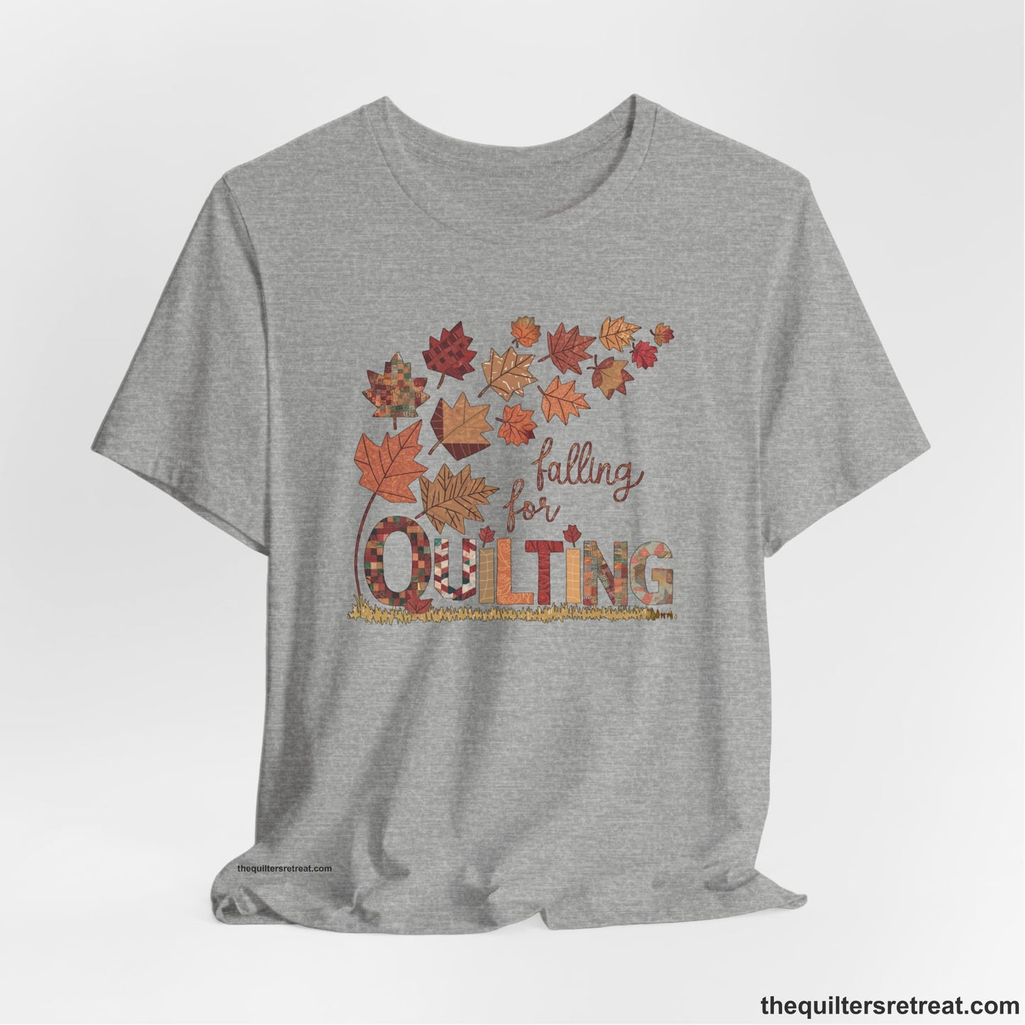 A Athletic Heather Short Sleeve T-Shirt with a falling autumn leaves and "Falling for Quilting" text in a patchwork style