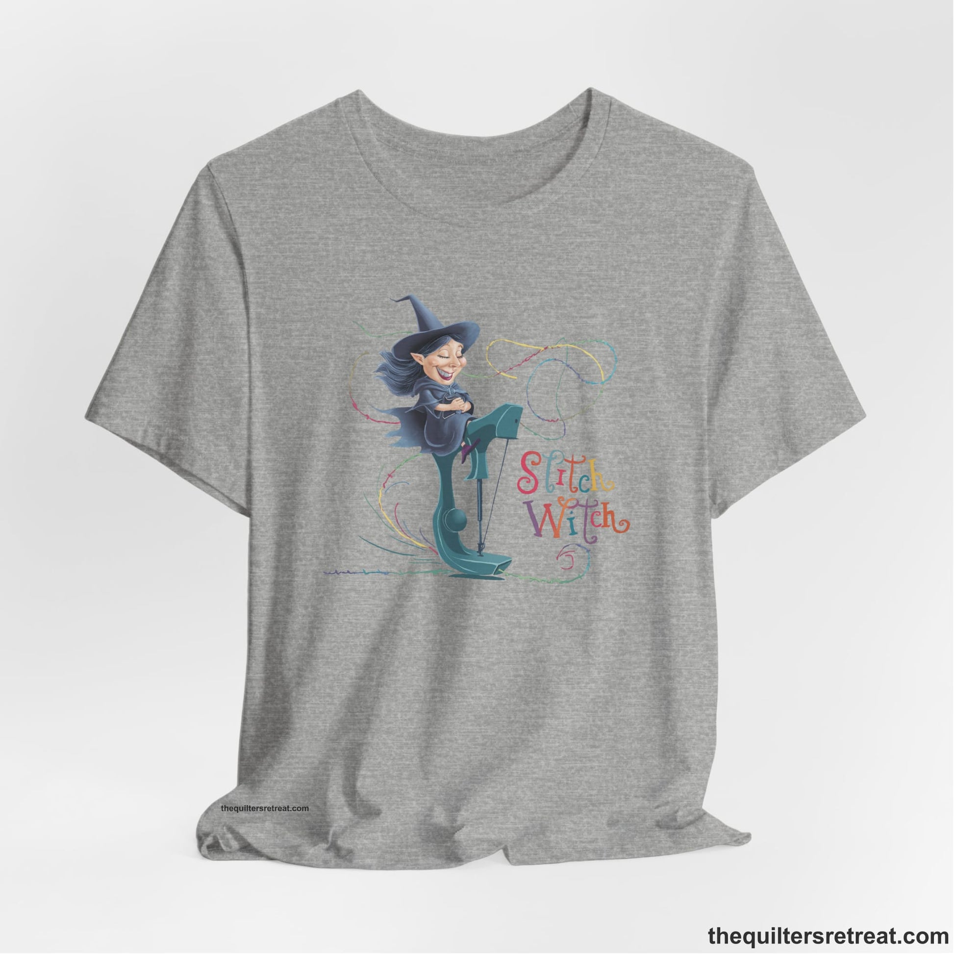 A Athletic Heather Short Sleeve T-Shirt with a witch on vintage sewing machine with "Stitch Witch" text in playful, colorful style