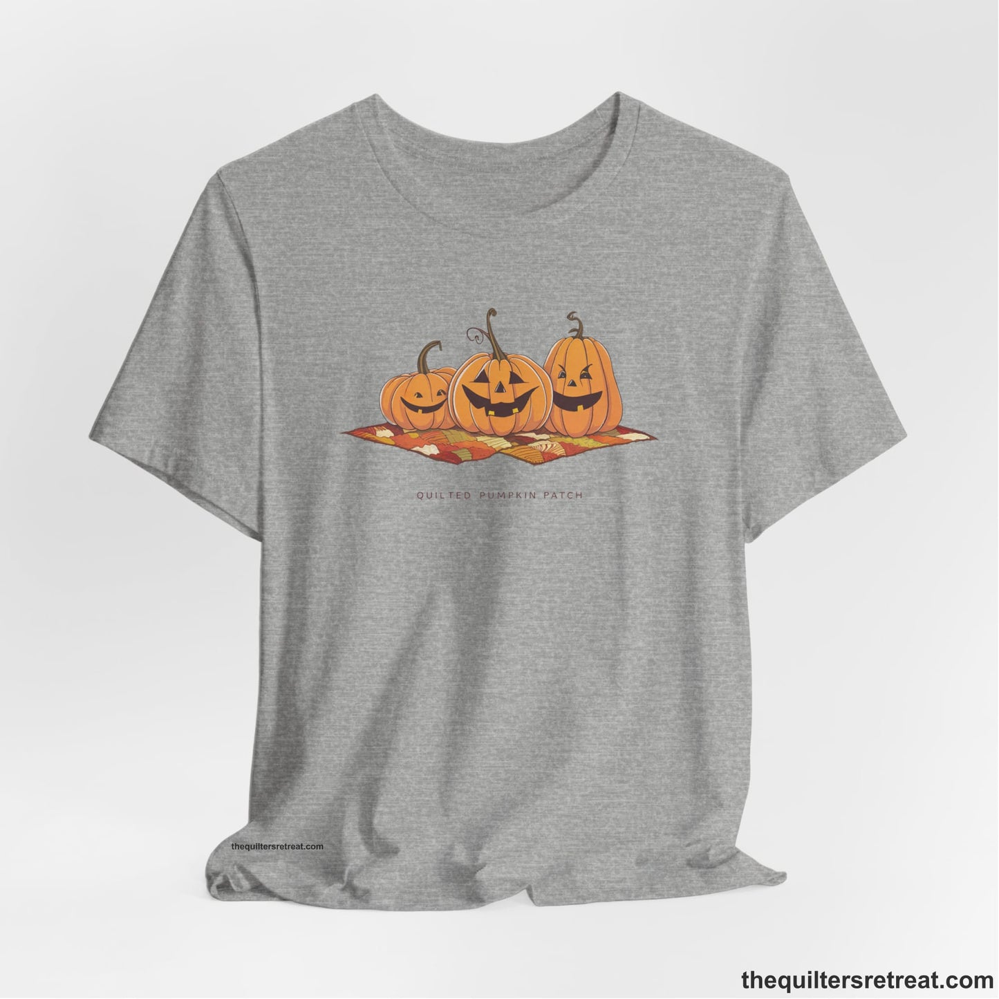 A Athletic Heather Short Sleeve T-Shirt with a playful jack-o'-lantern trio on a quilt with "Quilted Pumpkin Patch" text