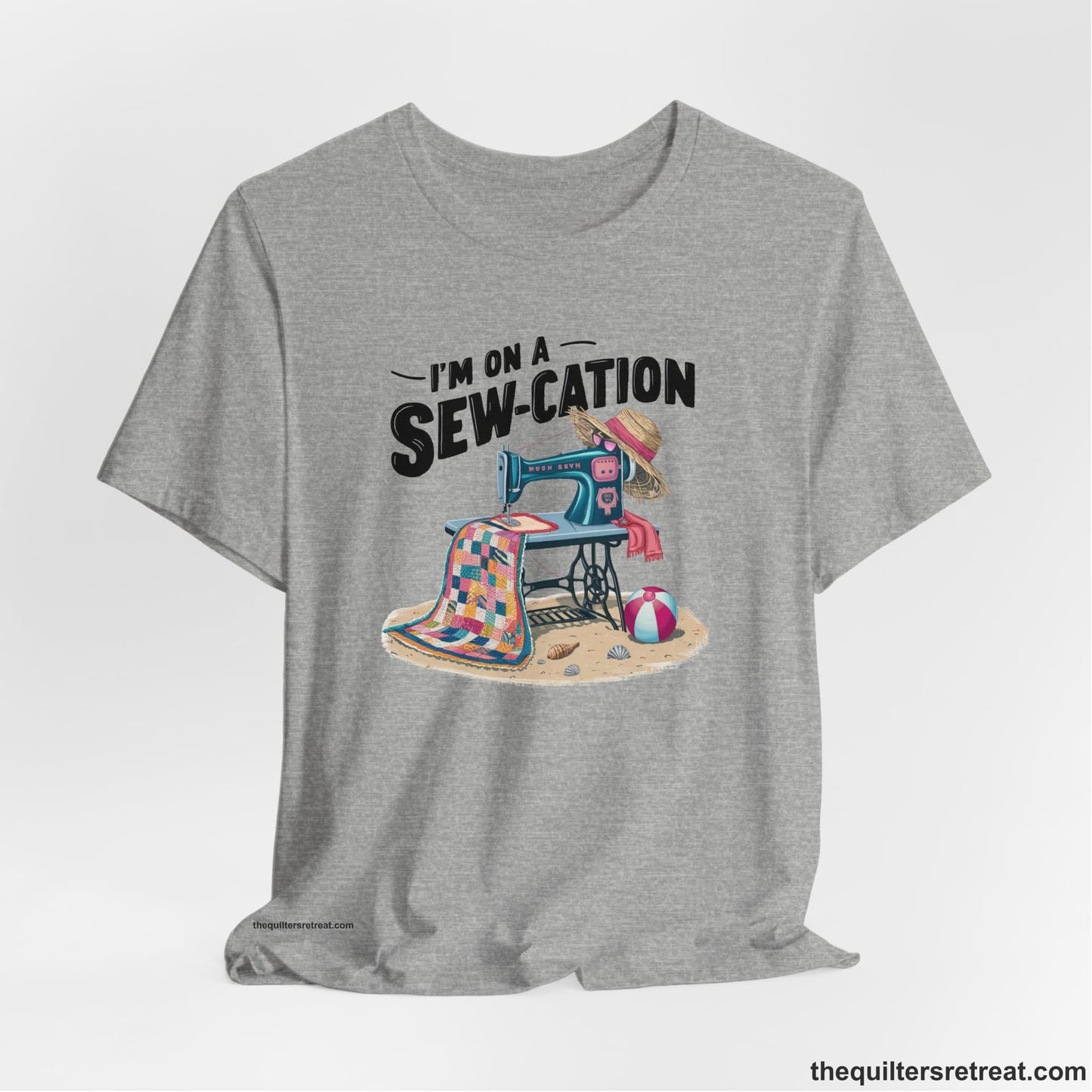 A Athletic Heather Short Sleeve T-Shirt with a vintage sewing machine with colorful quilt, beach items, and "I'm On A Sew-Cation" text