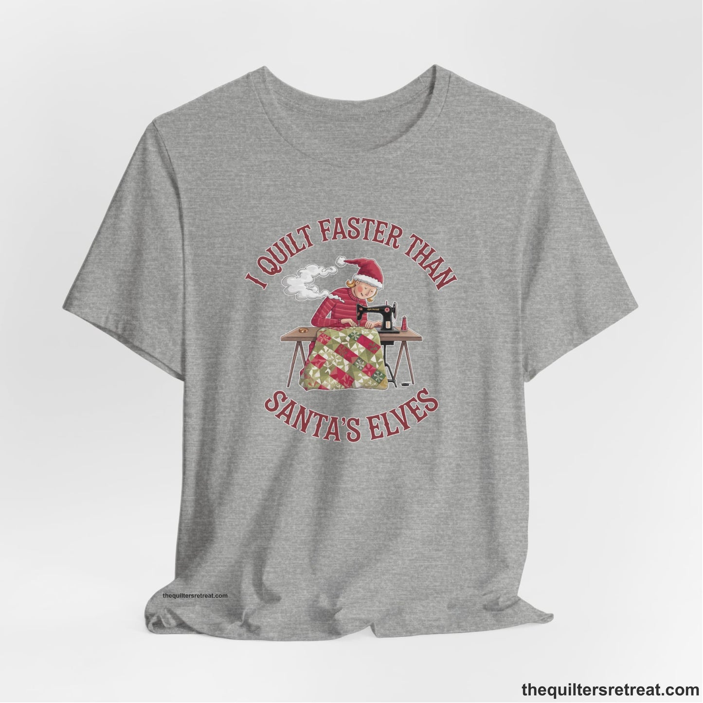 A Athletic Heather Short Sleeve T-Shirt with a whimsical illustration of a quilting woman with "I Quilt Faster Than Santa's Elves" text