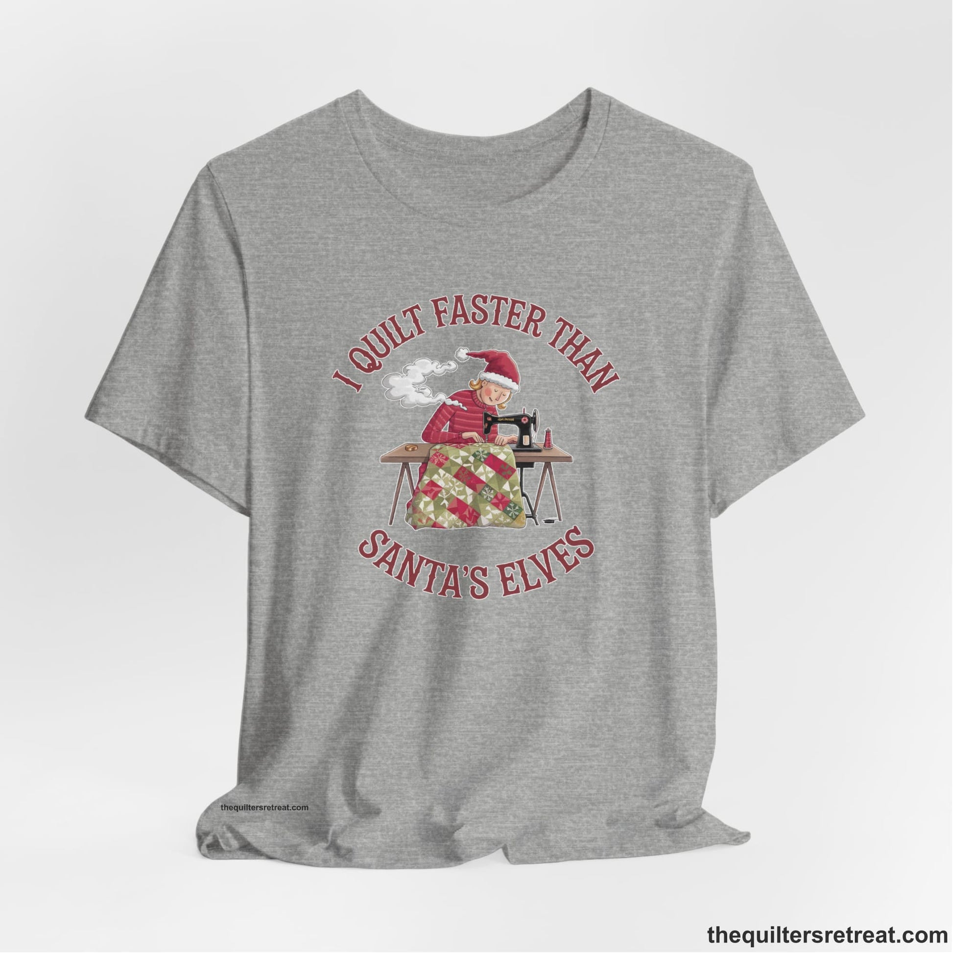 A Athletic Heather Short Sleeve T-Shirt with a whimsical illustration of a quilting woman with "I Quilt Faster Than Santa's Elves" text