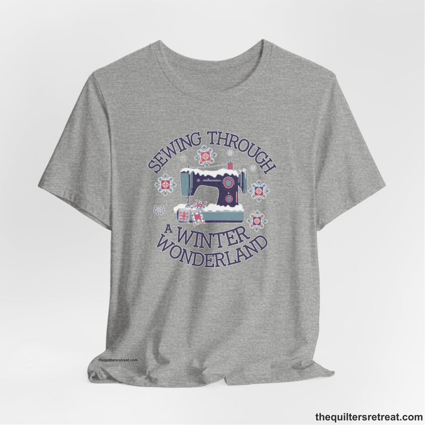 A Athletic Heather Short Sleeve T-Shirt with a sewing machine covered in snow with festive quilting elements and "Sewing Through a Winter Wonderland" text
