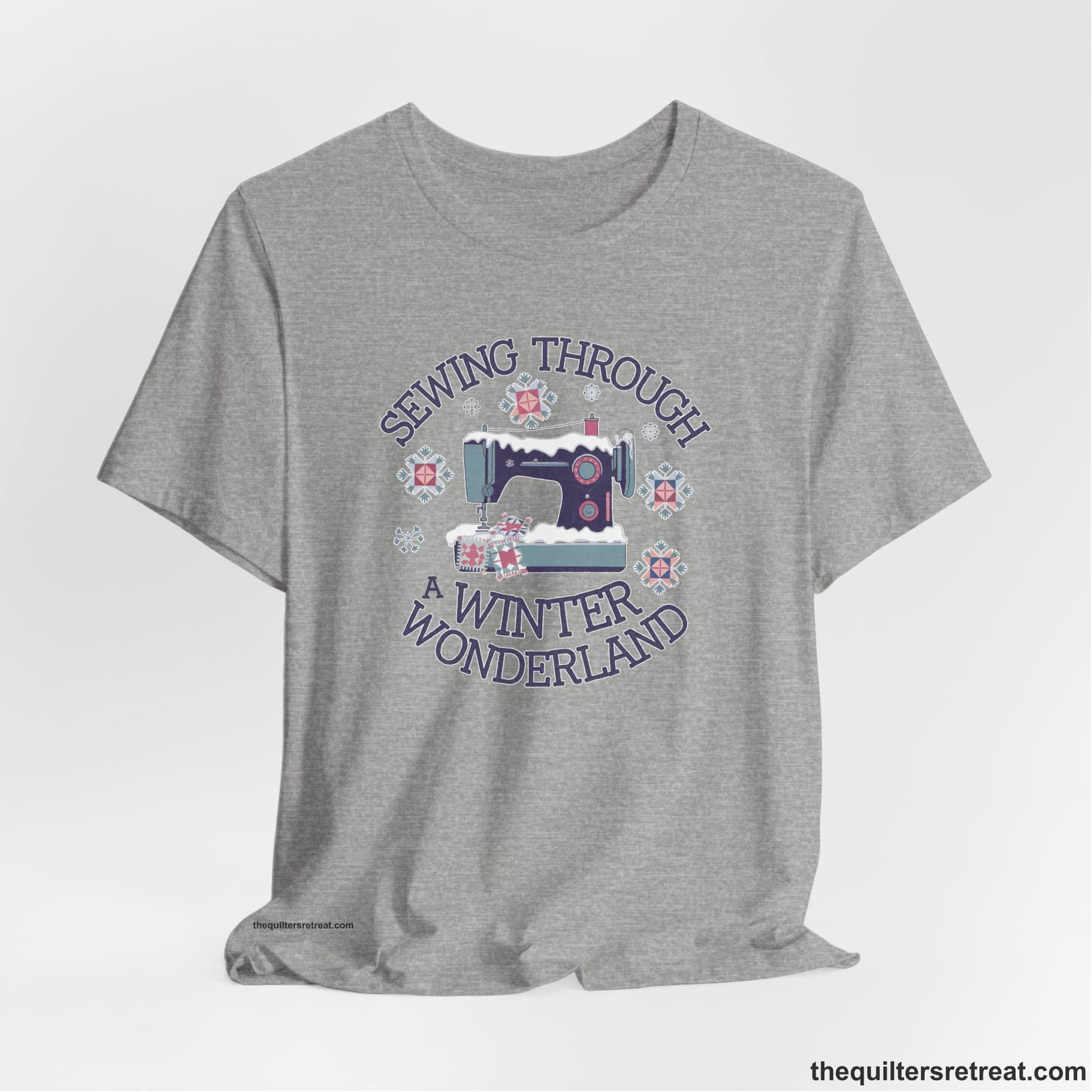A Athletic Heather Short Sleeve T-Shirt with a sewing machine covered in snow with festive quilting elements and "Sewing Through a Winter Wonderland" text