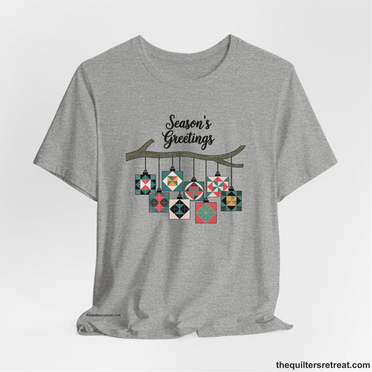 A Athletic Heather Short Sleeve T-Shirt with a season's greetings text above colorful quilt block ornaments on tree branch in rustic style