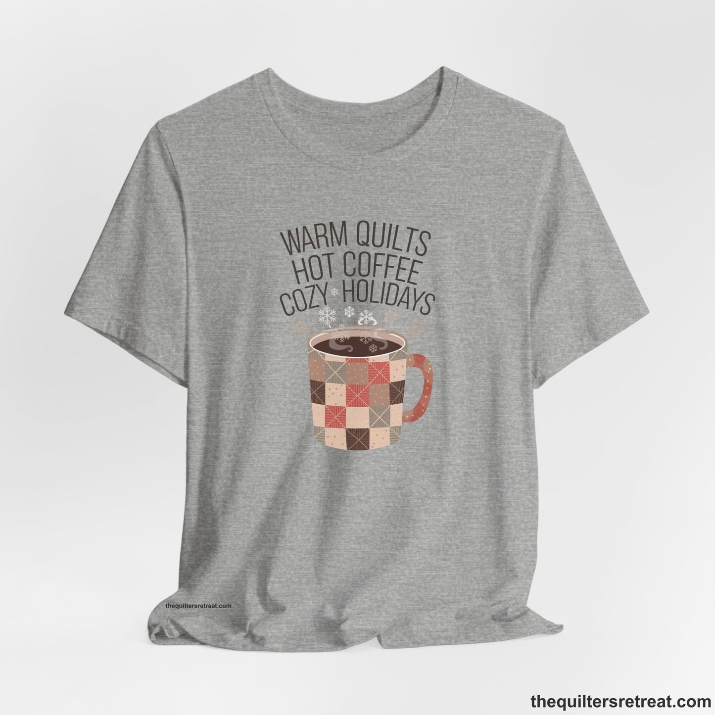 A Athletic Heather Short Sleeve T-Shirt with a warm quilts hot coffee cozy holidays text with a patchwork mug and snowflakes