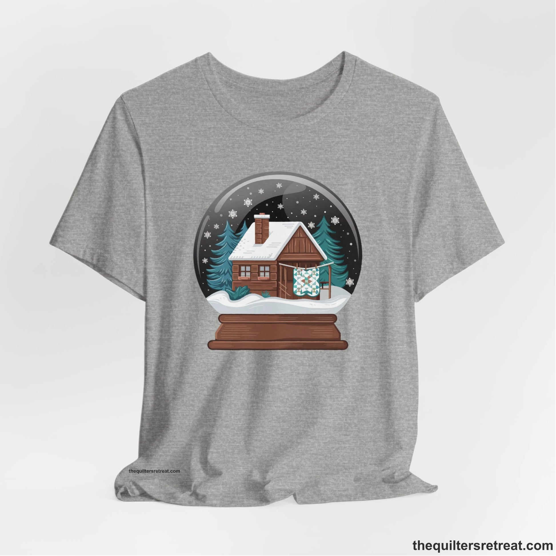 A Athletic Heather Short Sleeve T-Shirt with a cabin in a snow globe with snowflakes and trees, in a cozy rustic style