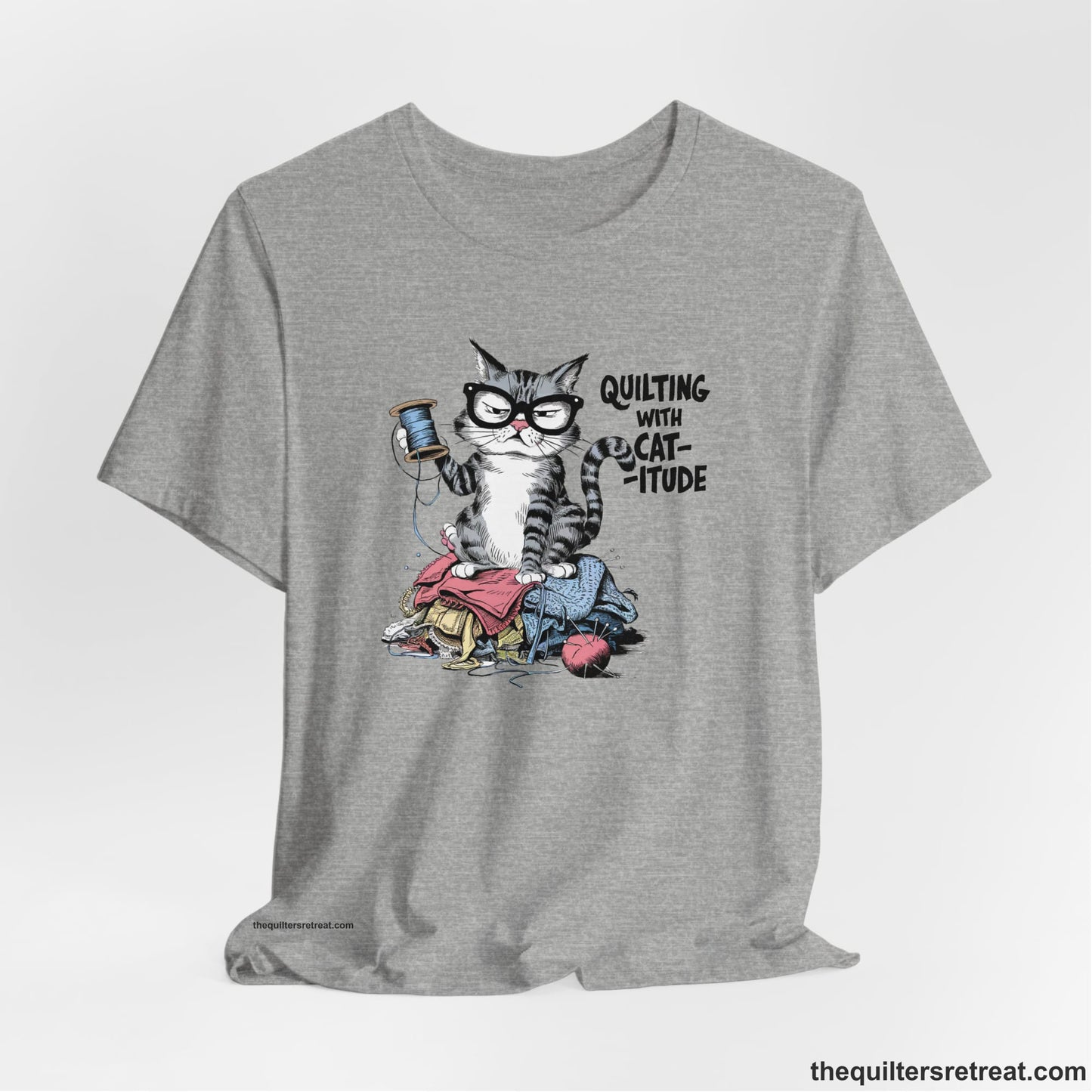 A Athletic Heather Short Sleeve T-Shirt with a grumpy cat holding thread spool atop fabric pile with "Quilting with Cat-itude" text