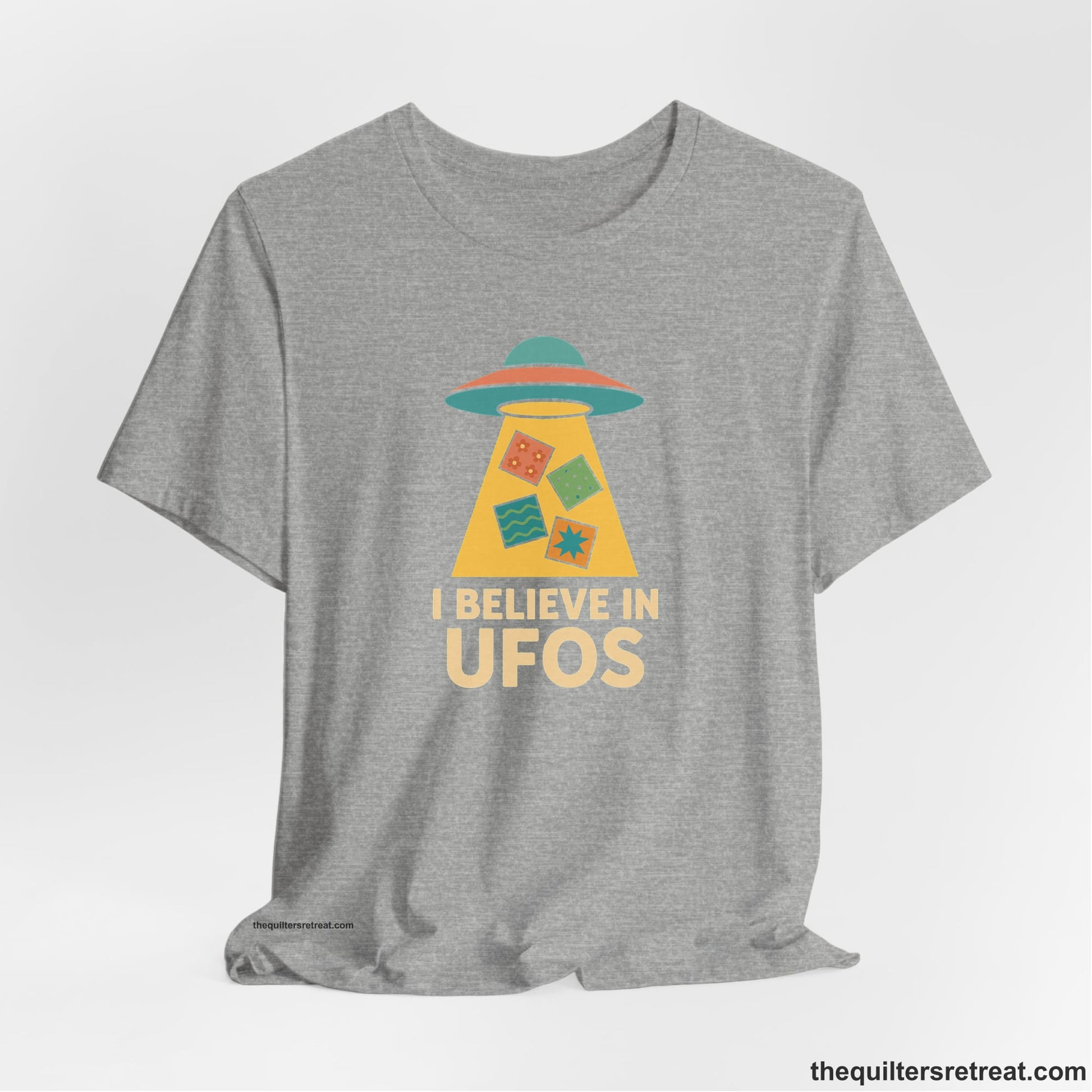 A Athletic Heather Short Sleeve T-Shirt with a colorful UFO with quilt patterns and bold "I Believe in UFOs" text in retro style