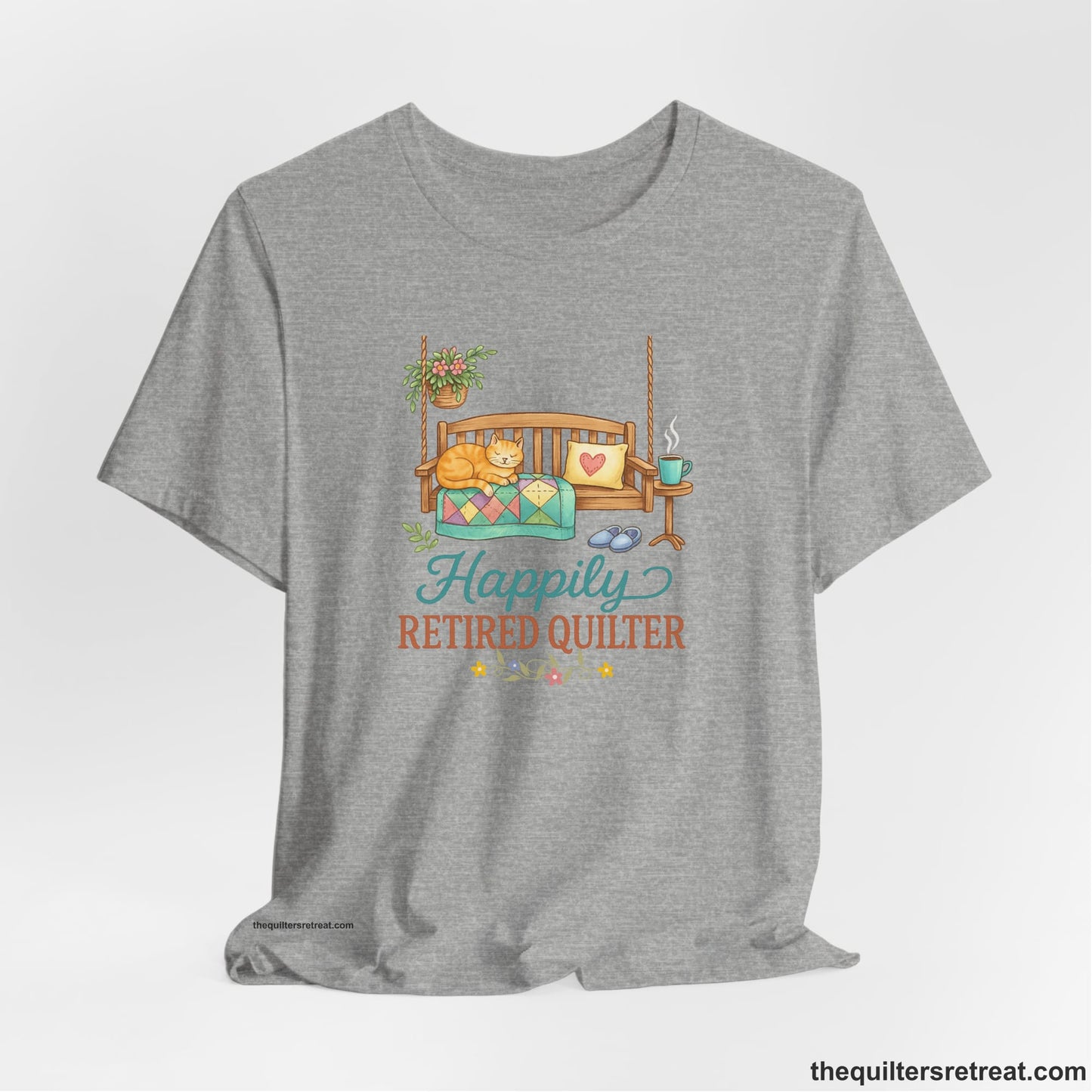 A Athletic Heather Short Sleeve T-Shirt with a hanging bench with cozy cat and quilt, surrounded by plants, "Happily Retired Quilter" text