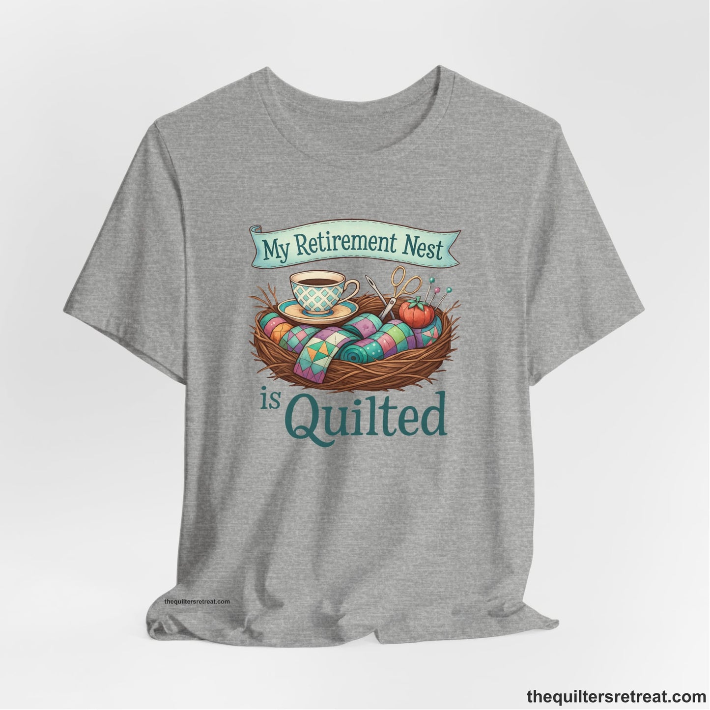 A Athletic Heather Short Sleeve T-Shirt with a My Retirement Nest is Quilted text with a cozy sewing elements illustration