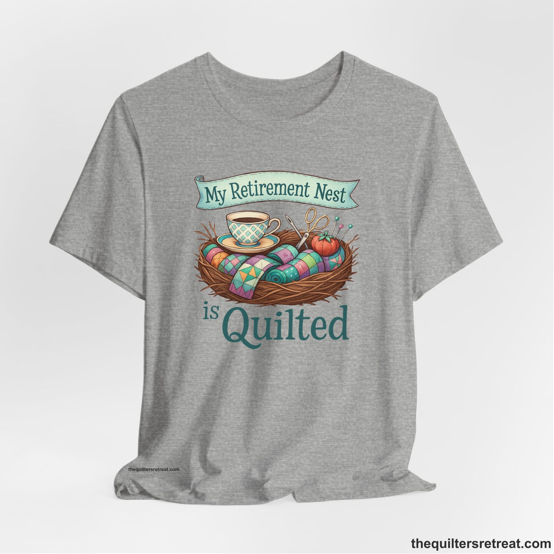 A Athletic Heather Short Sleeve T-Shirt with a My Retirement Nest is Quilted text with a cozy sewing elements illustration